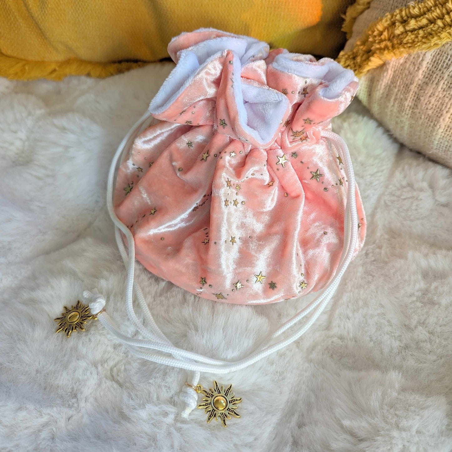 Pink starry multi-pocket dice bag with gold stars, velvety fabric, and solar charm drawstrings, on a plush surface.
