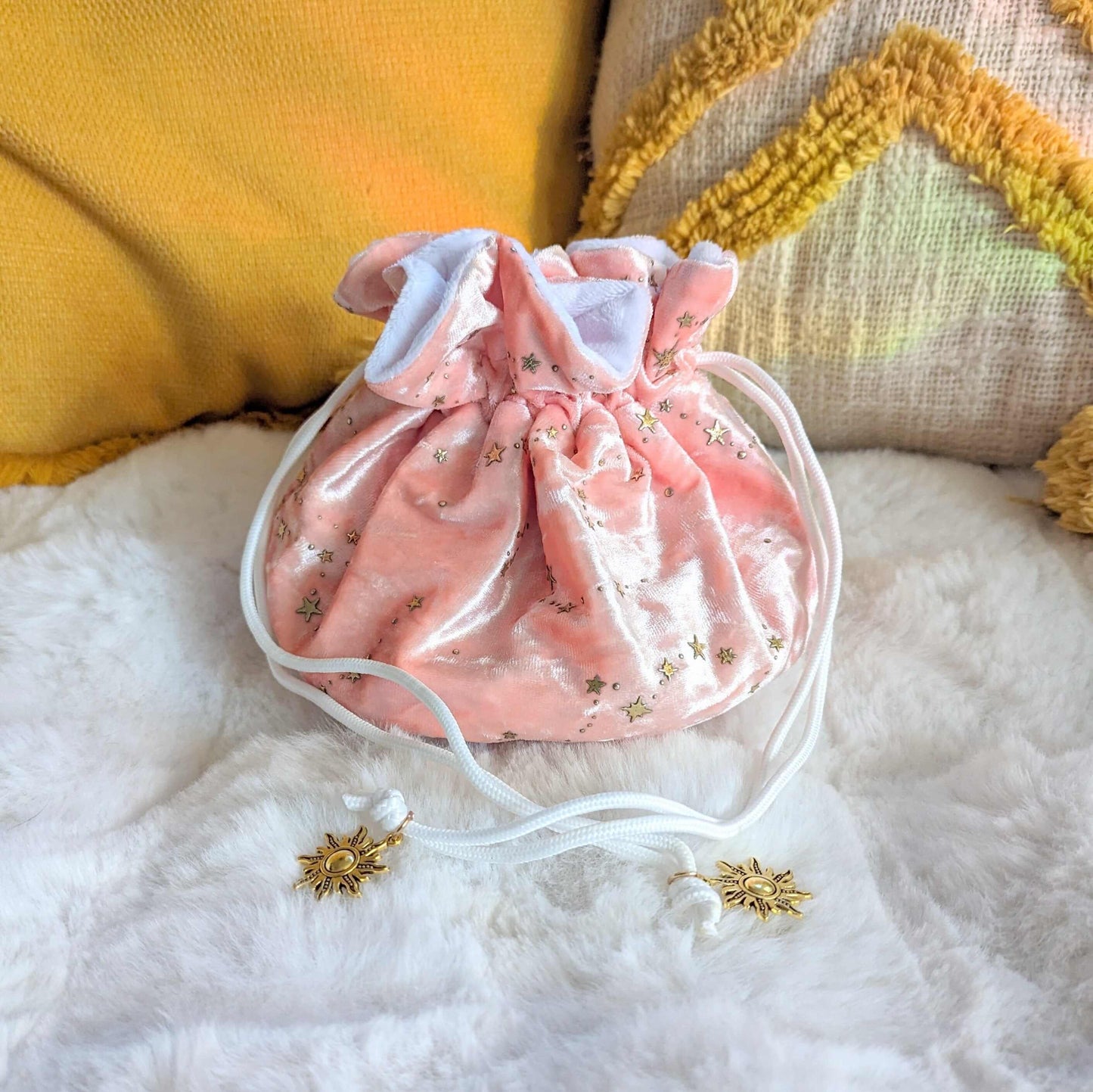 Pink velvety dice bag with gold star pattern and solar charms, soft fabric, multi-pocket design, and white cord drawstrings.