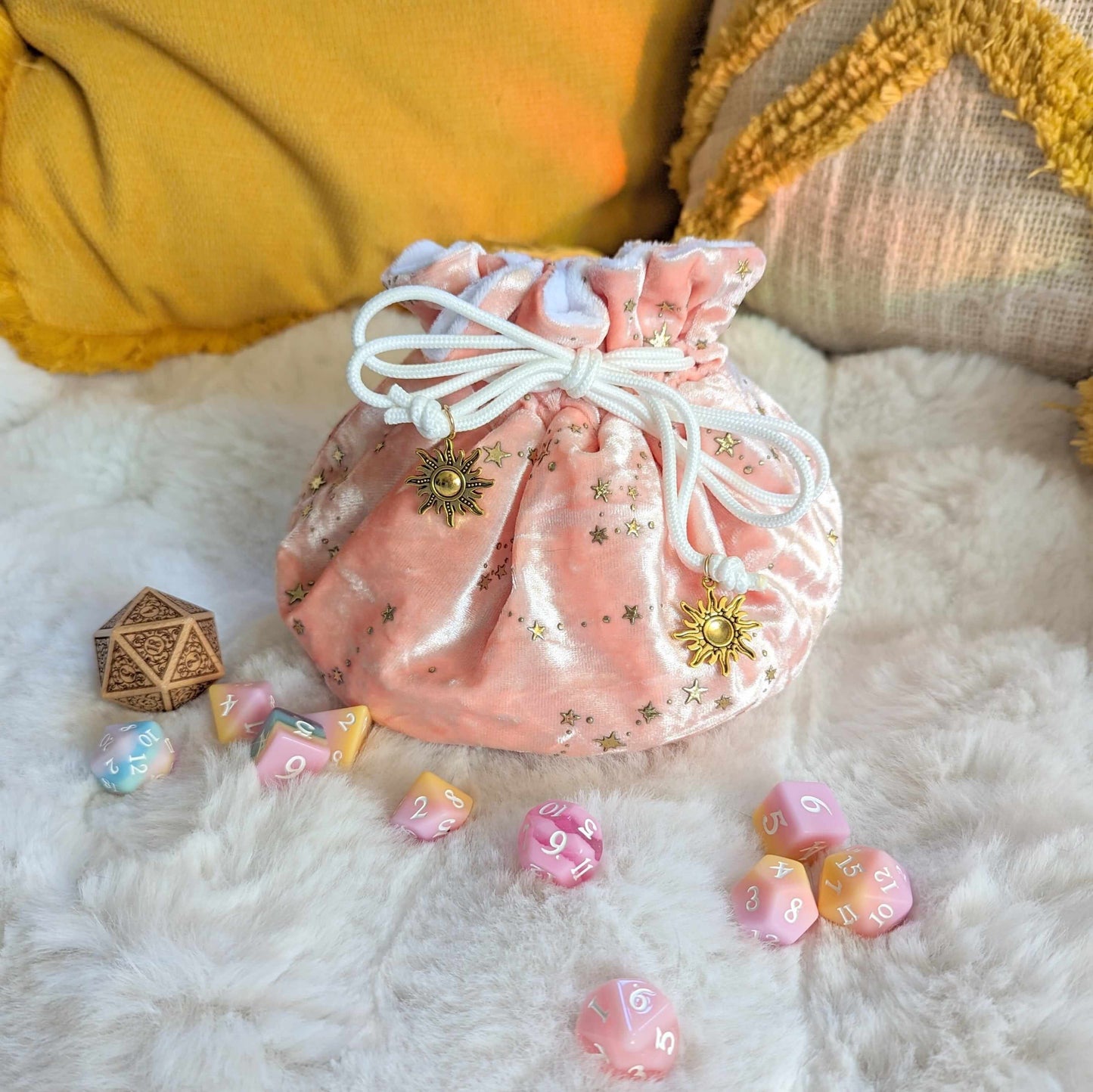 Starry pink multi-pocket dice bag with gold star design and drawstrings on a cozy surface, surrounded by colorful dice.