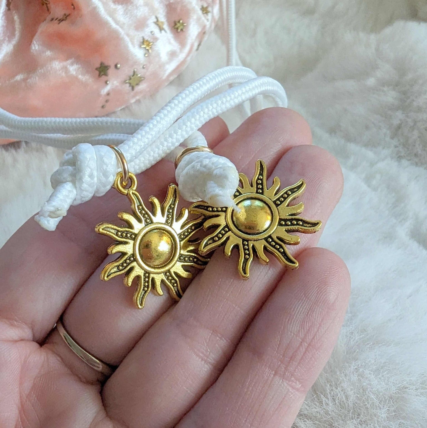 Close-up of a pink dice bag with gold starry prints, white drawstrings, and gold solar charms displayed on a hand.