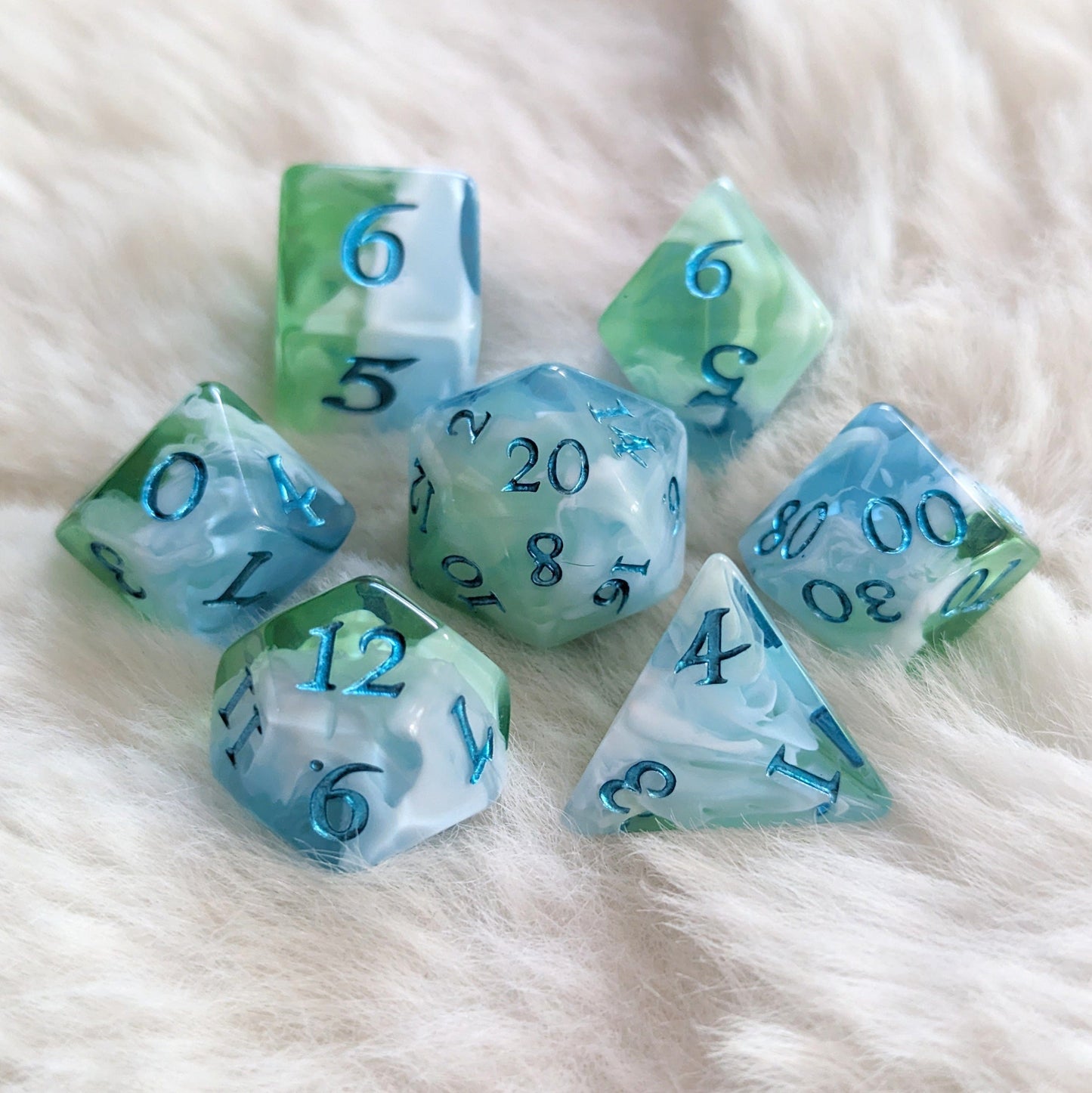 Tidecaller Dice Set with light blue, opaque white, and green dice featuring metallic teal numbers, resting on soft fabric.