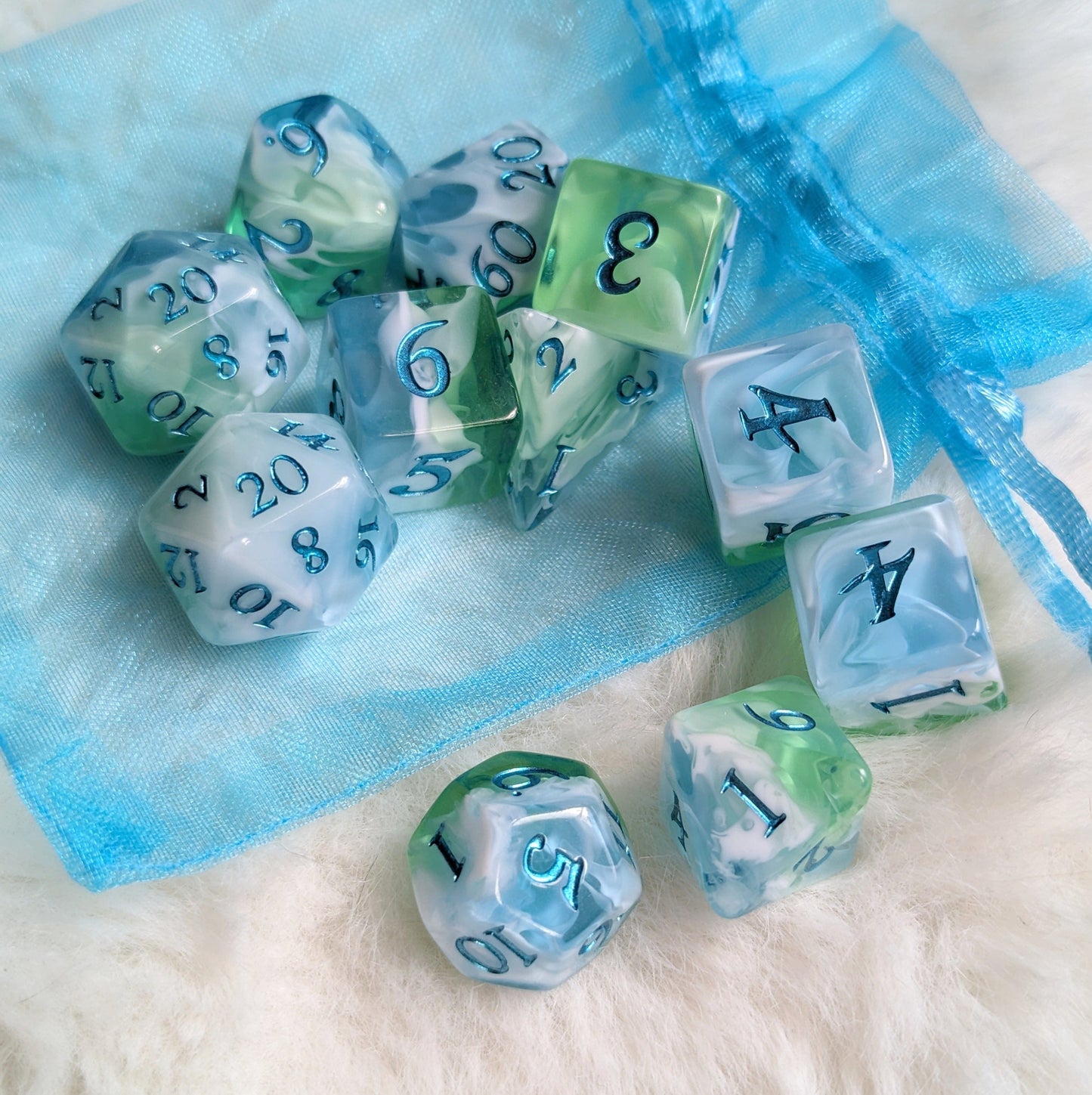 Tidecaller Dice Set in light blue, white, and green with metallic teal numbers on a blue drawstring bag.