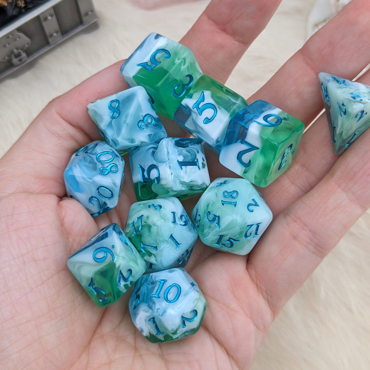 Hand holding Tidecaller Dice Set in light blue, white, and green with metallic teal numbers for tabletop RPG games.