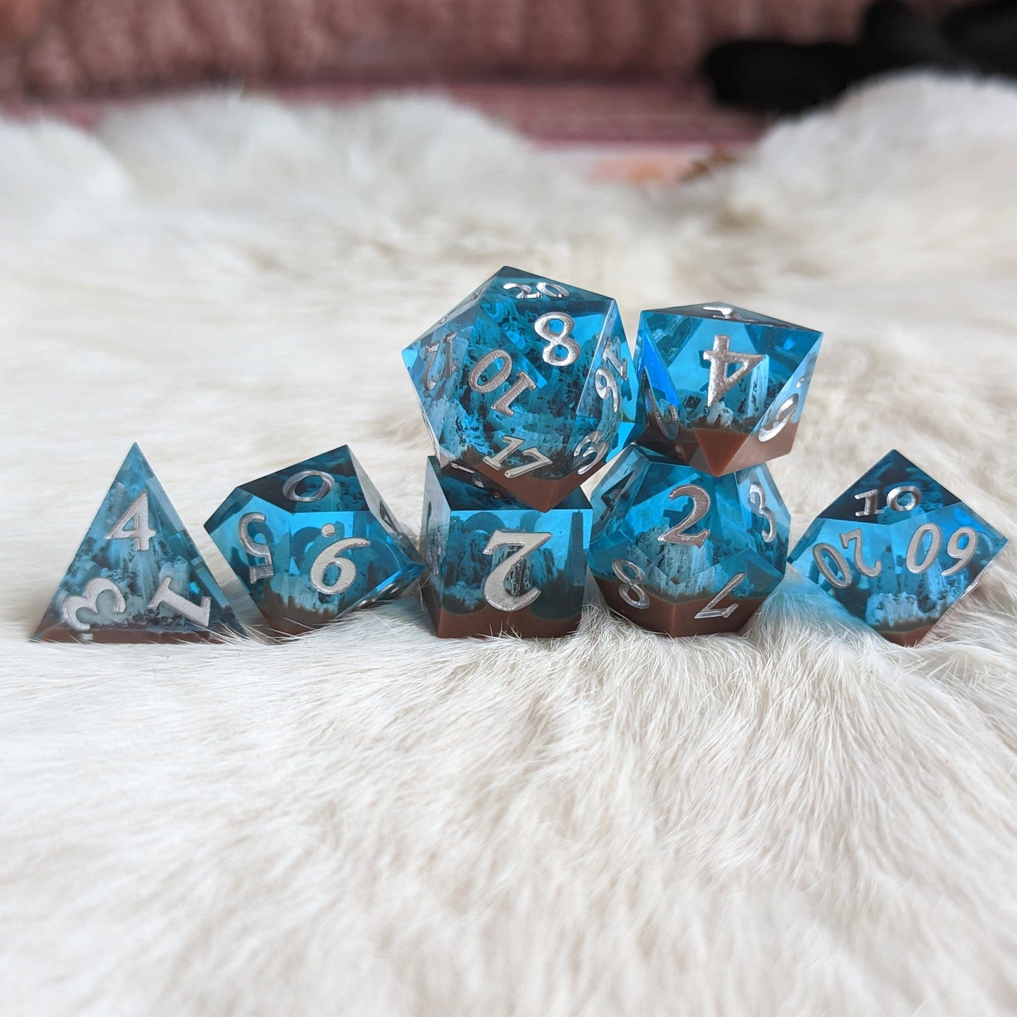 Tundra Peak Sharp Edge Resin DnD Dice Set with blue and brown mountain design displayed on a soft white fur background.