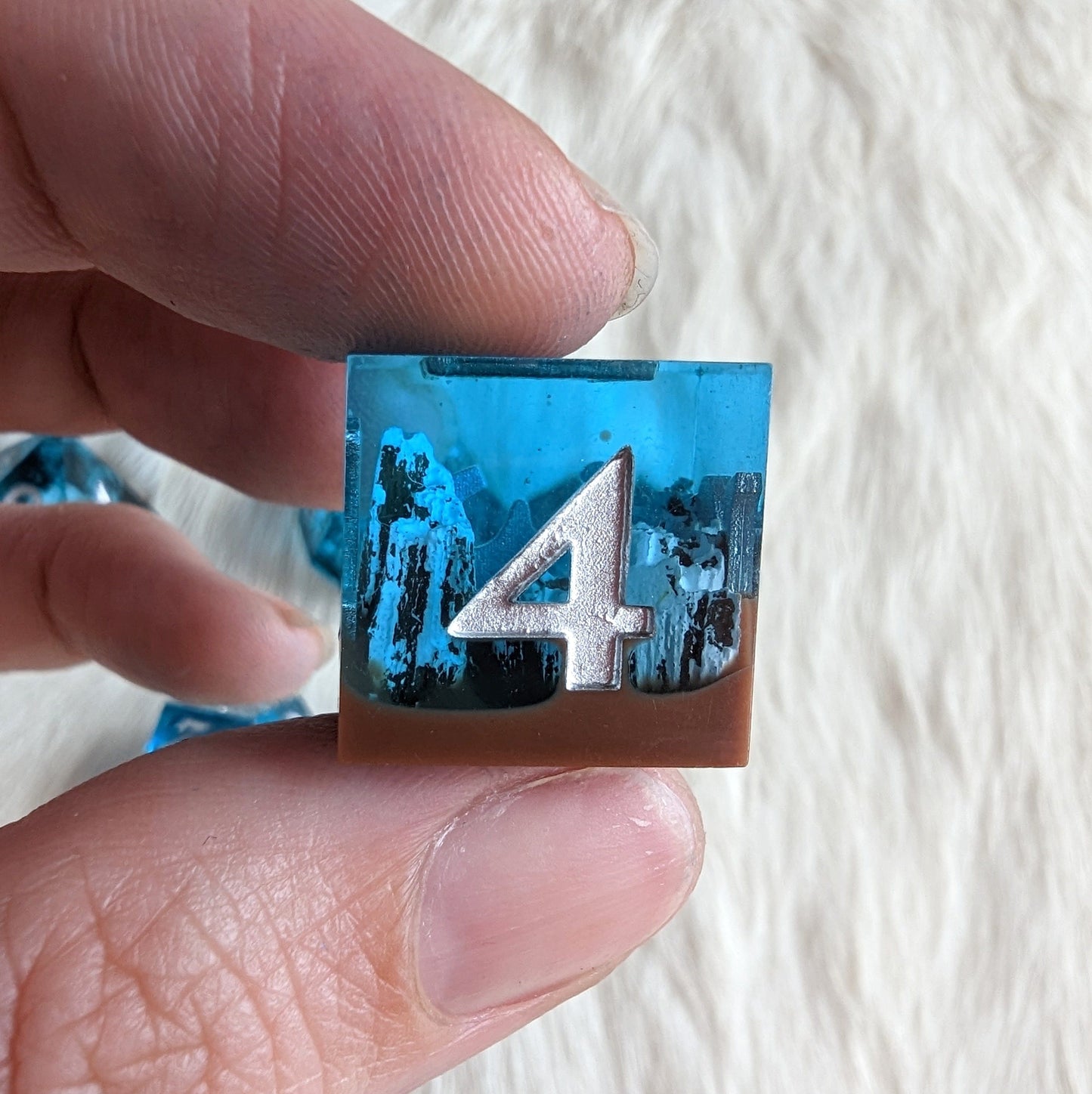 Hand holding Tundra Peak Sharp Edge Resin DnD dice with mountain design and number four, ideal for tabletop role-playing games.