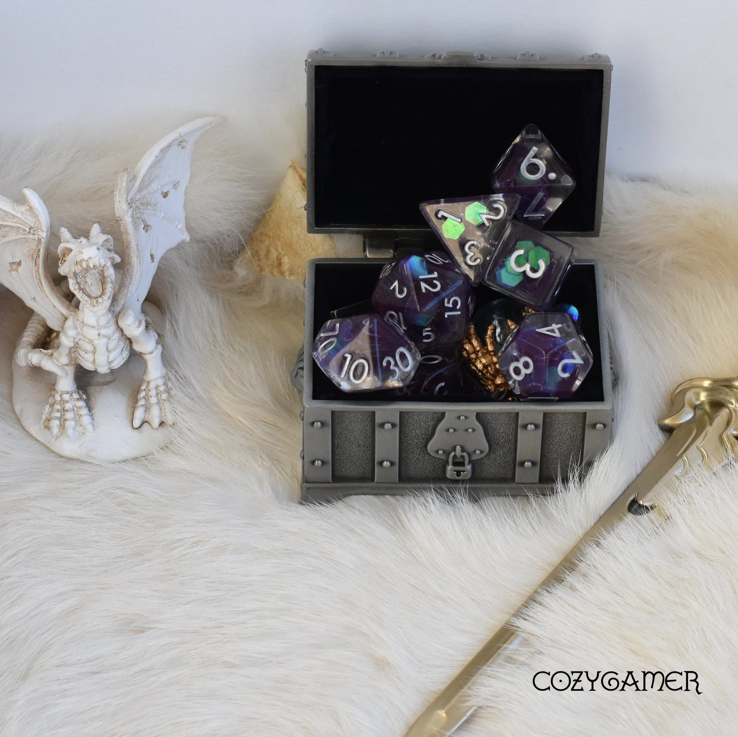 Amethyst Glint Dice Set in a treasure chest with a dragon figurine on a furry surface, ideal for tabletop RPGs.