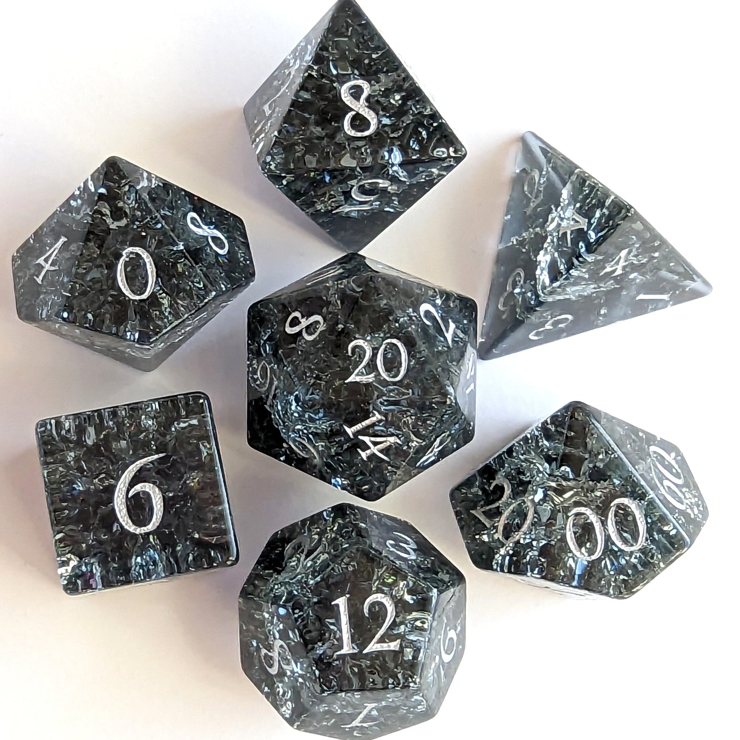 Black and blue crackled glass dice set of seven for tabletop games, including d20, displaying intricate designs and numbers.