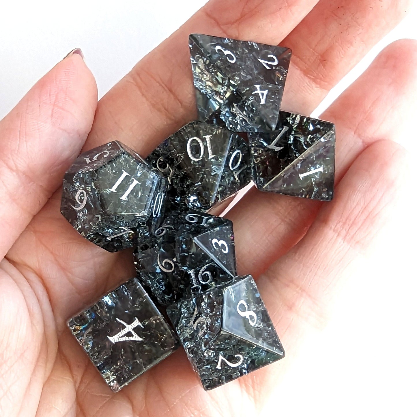 Black and blue crackled glass dice set in hand, featuring seven DnD pieces including d20 and d12 dice.