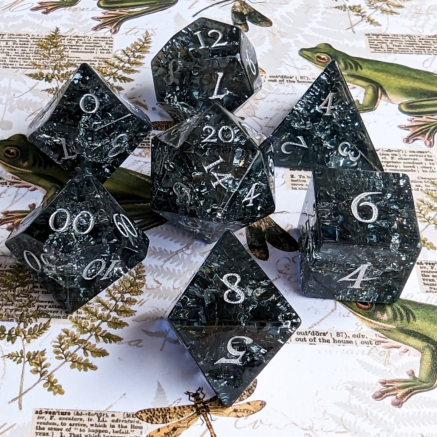 Black and blue crackled glass dice set with seven pieces on a nature-themed background. Ideal for DnD games.