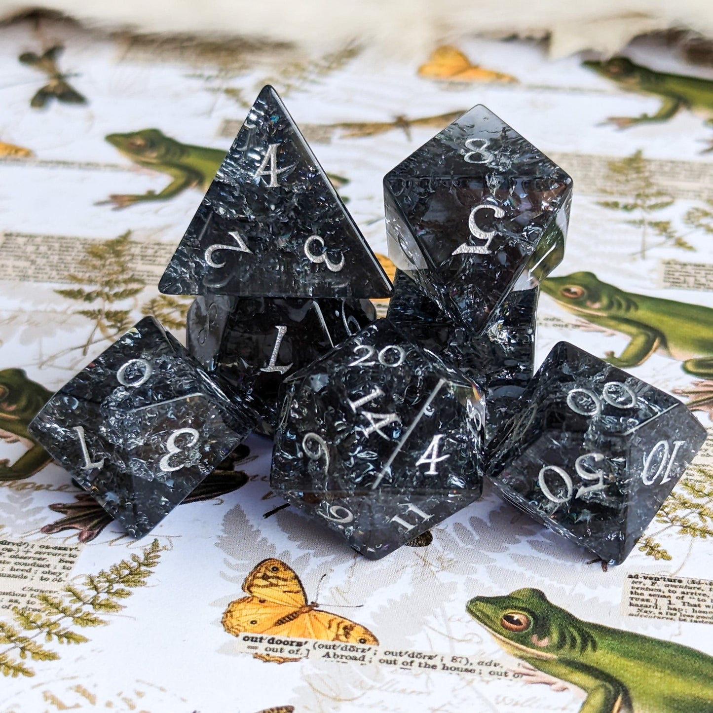 Black and blue crackled glass dice set with seven pieces, perfect for DnD games, displayed on a nature-themed background.