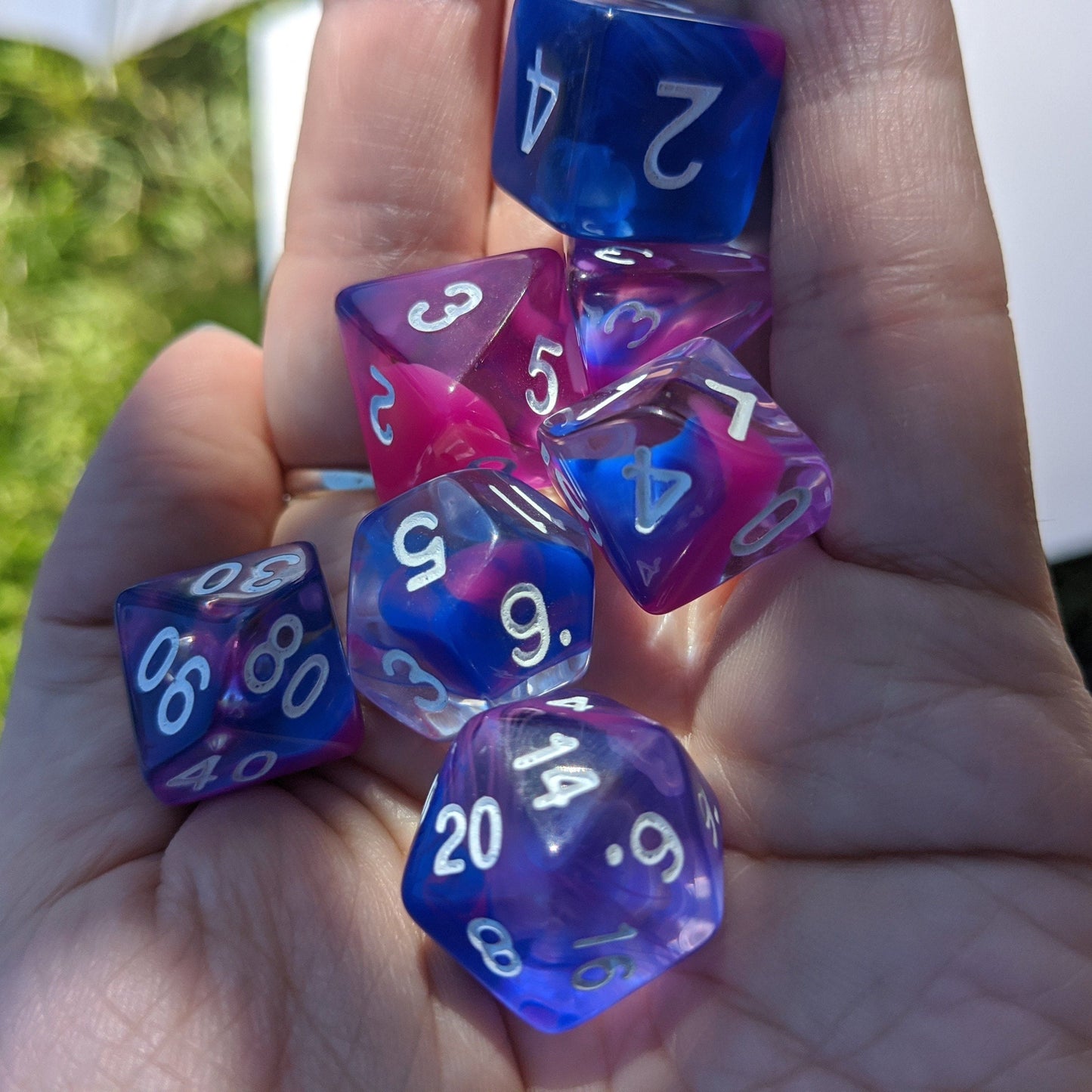 Blue and pink marble dice set for TTRPG, including D20, D12, D10, D%, D8, D6, D4, held in hand.