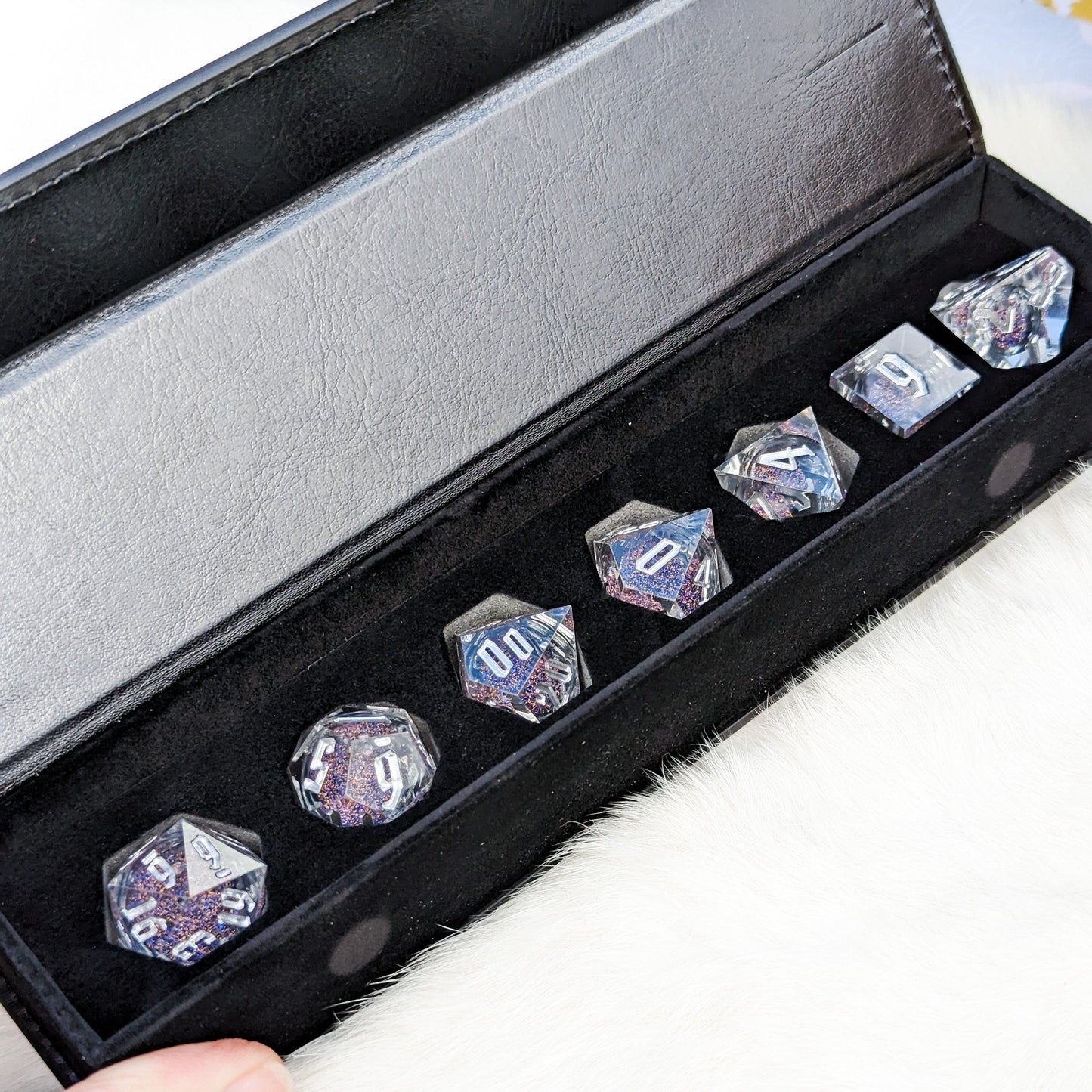 Black case with a set of seven polyhedral dice featuring a clear liquid core with blue and gold glitter for tabletop RPGs.