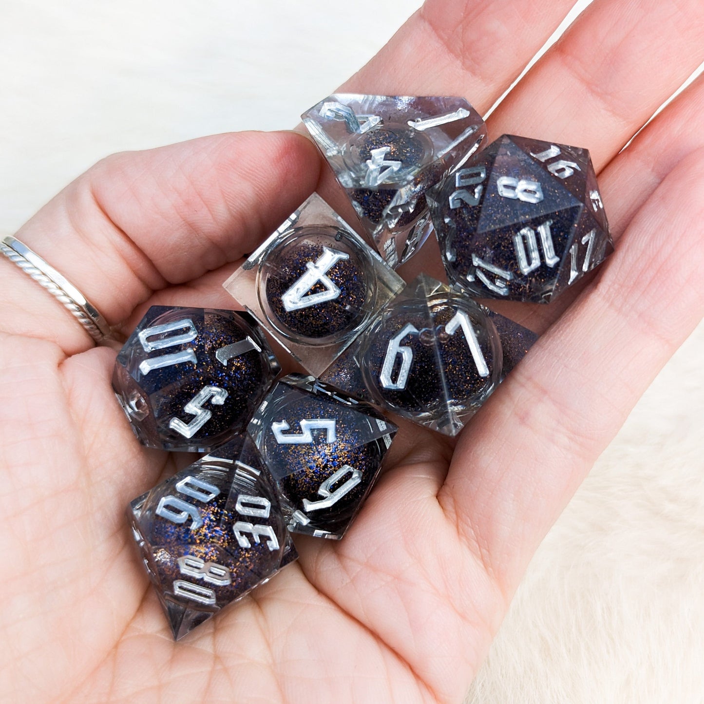 Hand holding a clear resin DnD dice set with blue and gold glitter liquid core and sharp edges, perfect for tabletop role-playing games.