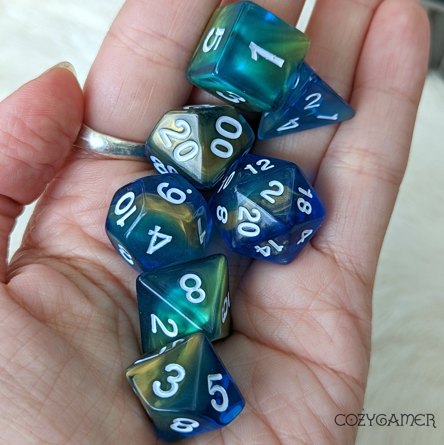 "Blue Beaches marbled polyhedral dice set with blue and gold hues for tabletop RPGs in a hand."