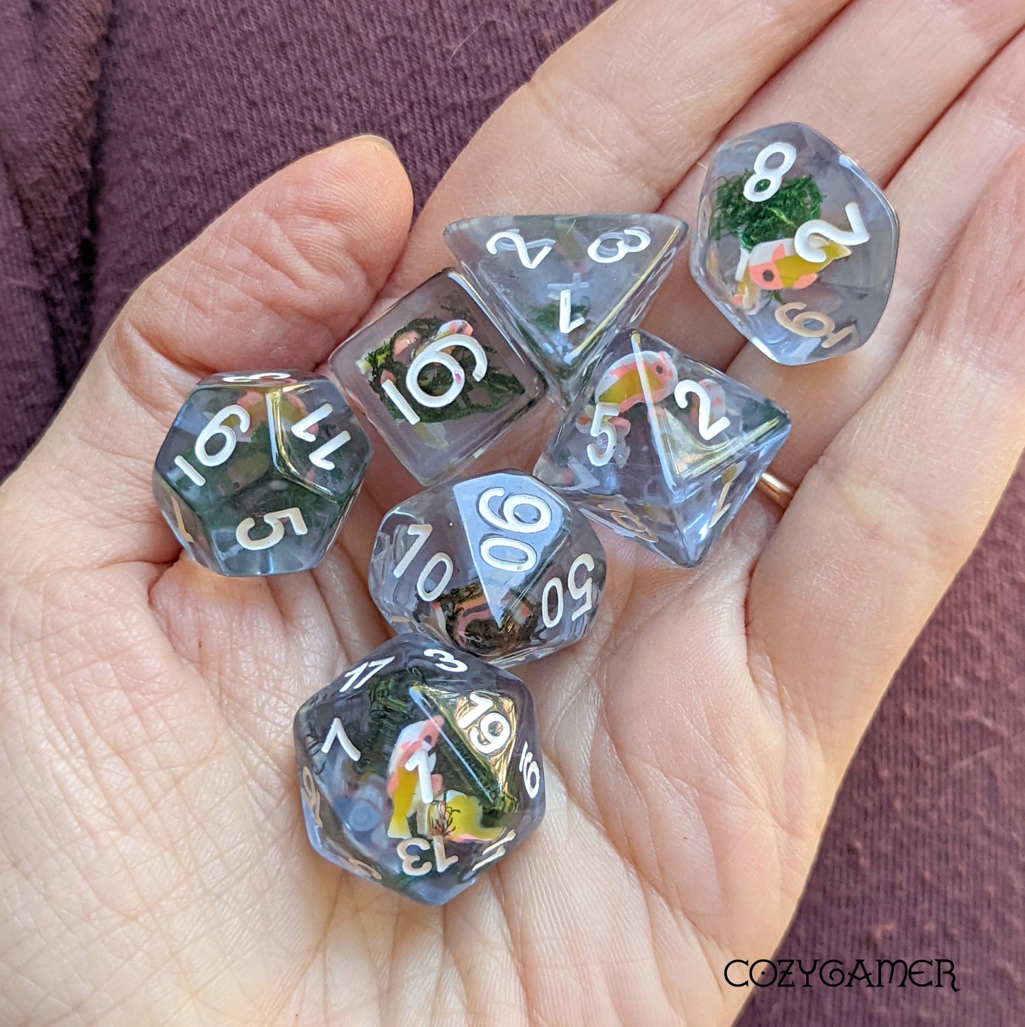 Hand holding Blue Swimming Fish DnD dice set with fish and moss inside, perfect for tabletop games like Dungeons and Dragons.