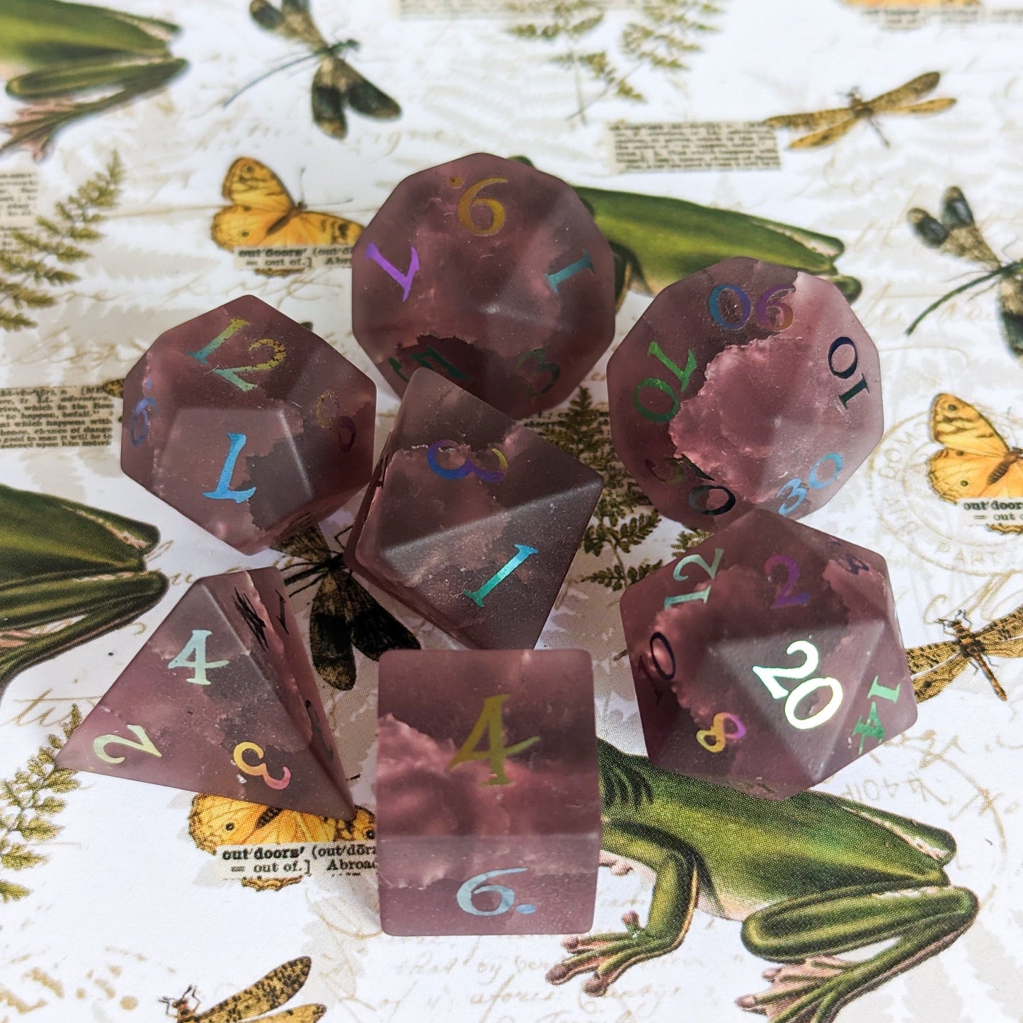 Burgundy crackled glass dice set featuring seven polyhedral dice for tabletop RPGs, displayed on a nature-themed background.