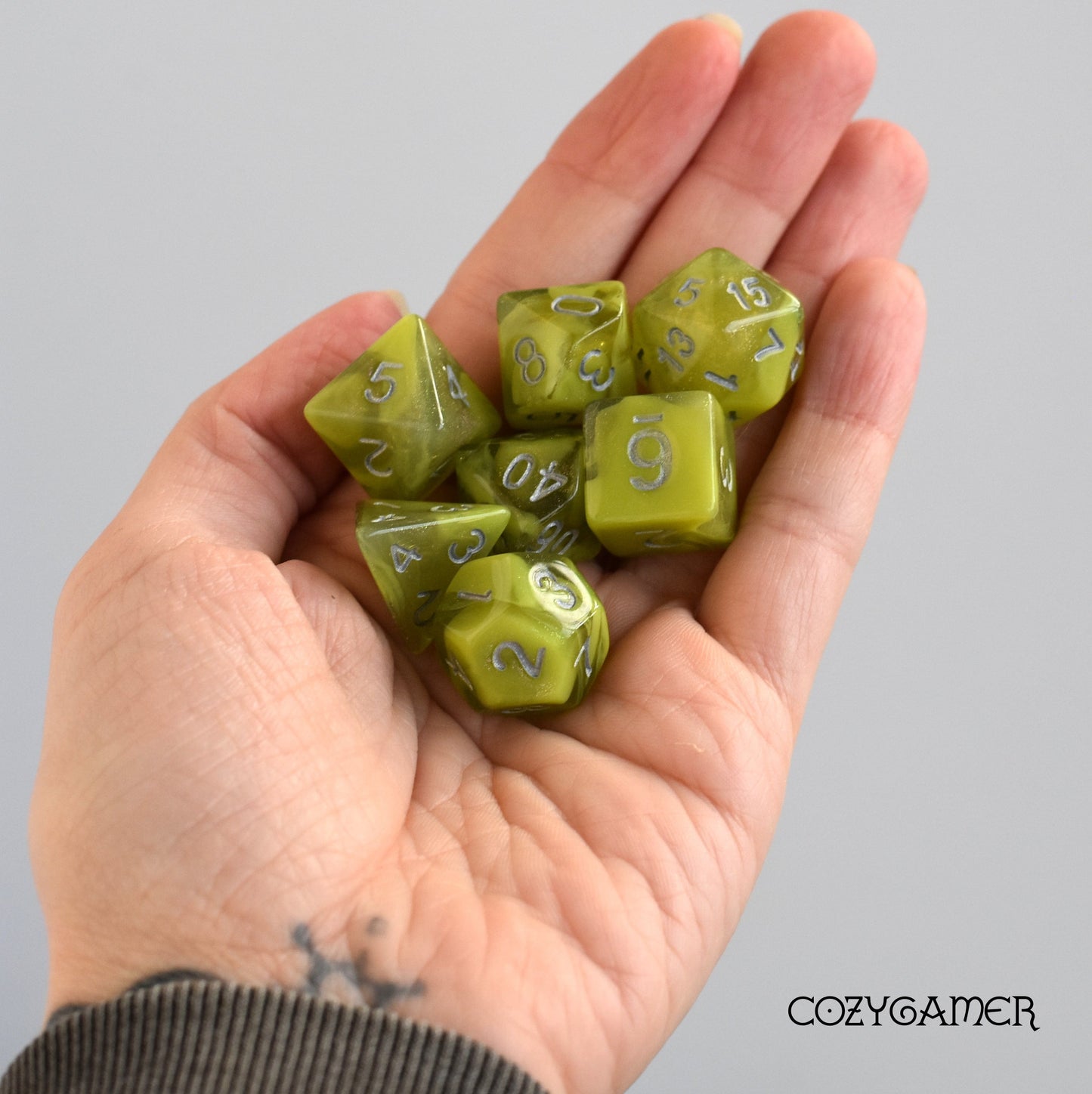 Hand holding Cave Slime Dice Set, 7-piece green glitter acrylic dice for TTRPG games like Dungeons and Dragons.