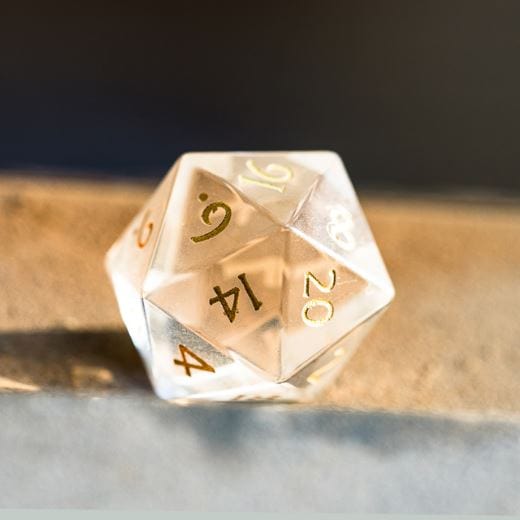 Clear Glass Dice with Gold Font on Tabletop, Part of a 7 Piece TTRPG Dice Set in Felt Hexagonal Box.