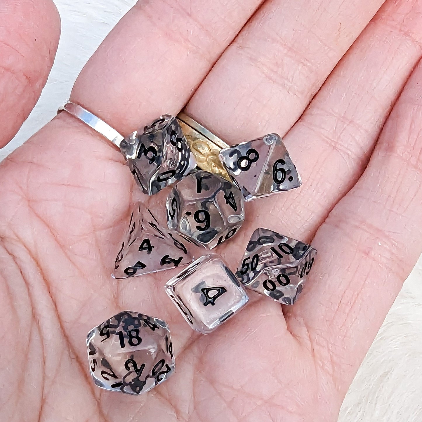 Clear mini polyhedral DND dice set held in hand, including D4, D6, D8, D10, D100, D12, D20, showcasing size and readability.