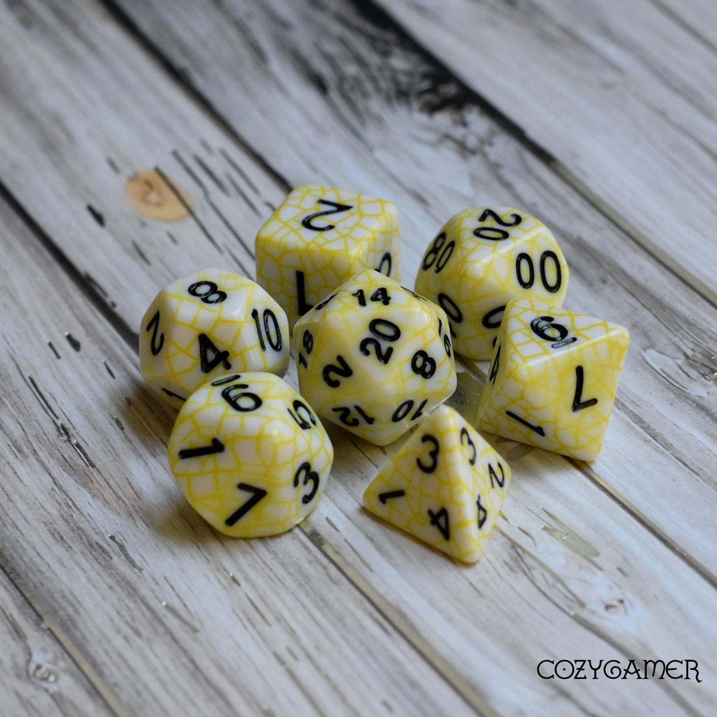 Cracked Porcelain DnD polyhedral dice set in white with yellow web pattern on wooden surface, ideal for tabletop role-playing games.