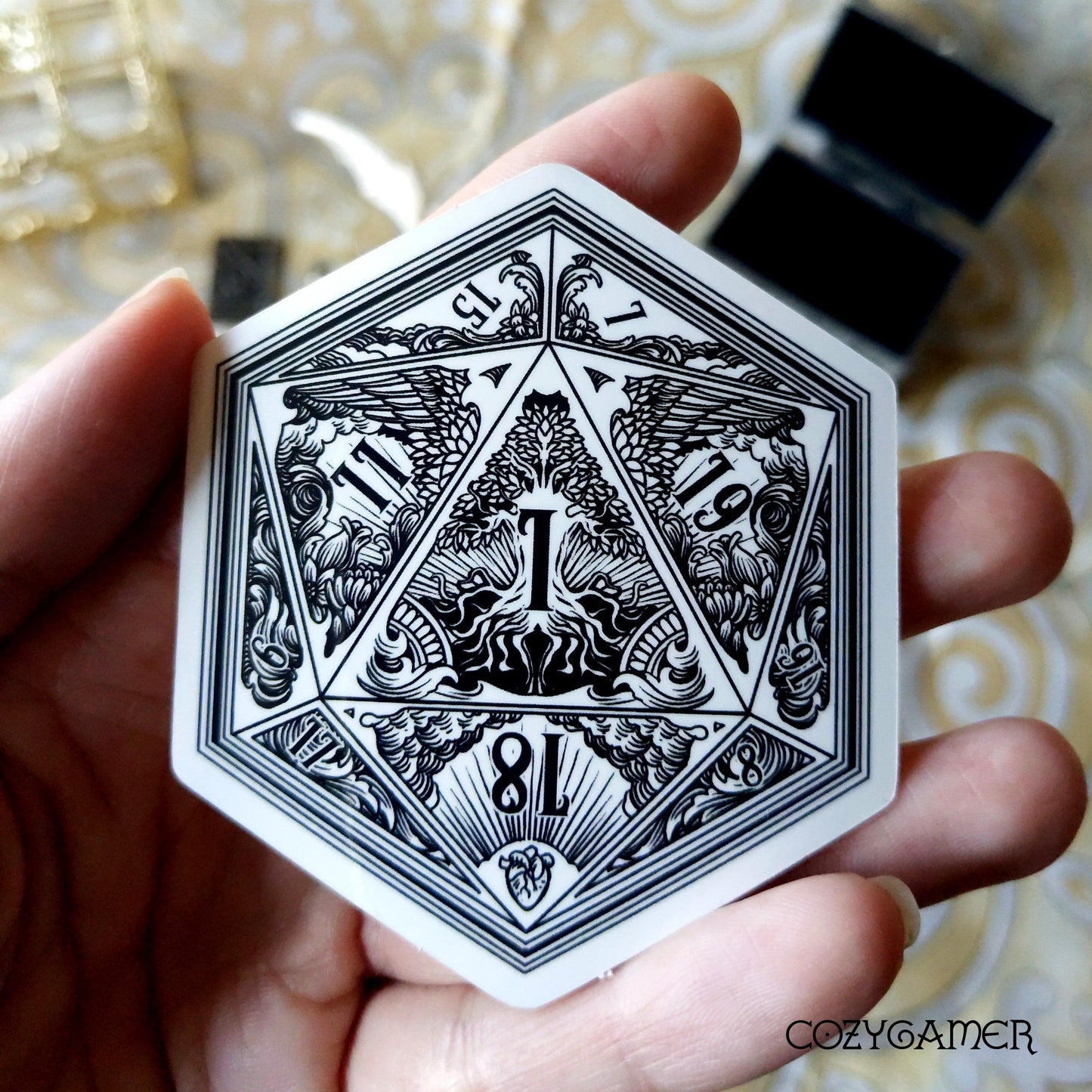 Hand holding D20 DND dice sticker with intricate life and death TTRPG design featuring trees and waves.