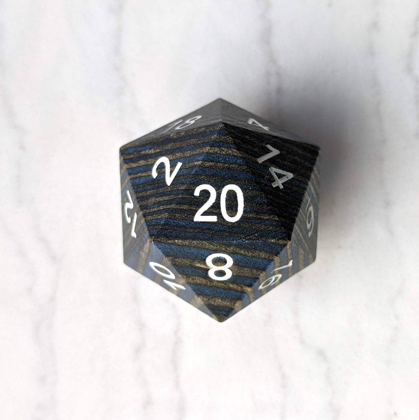 Dark blue and grey striped large wooden D20 dice on a marble background, ideal for collectors and gaming enthusiasts.