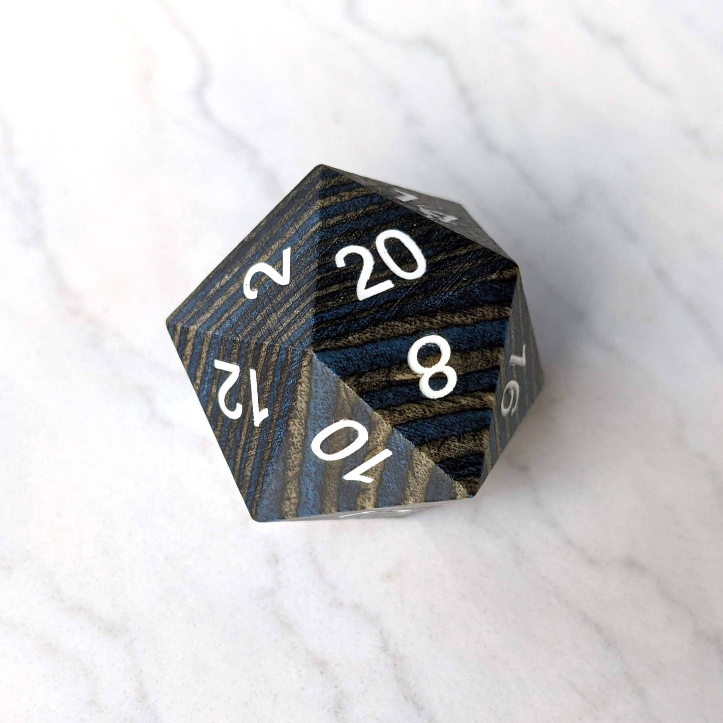 Dark blue and grey wood stripe large wooden D20 dice on a marble surface, perfect for collectors and gaming enthusiasts.