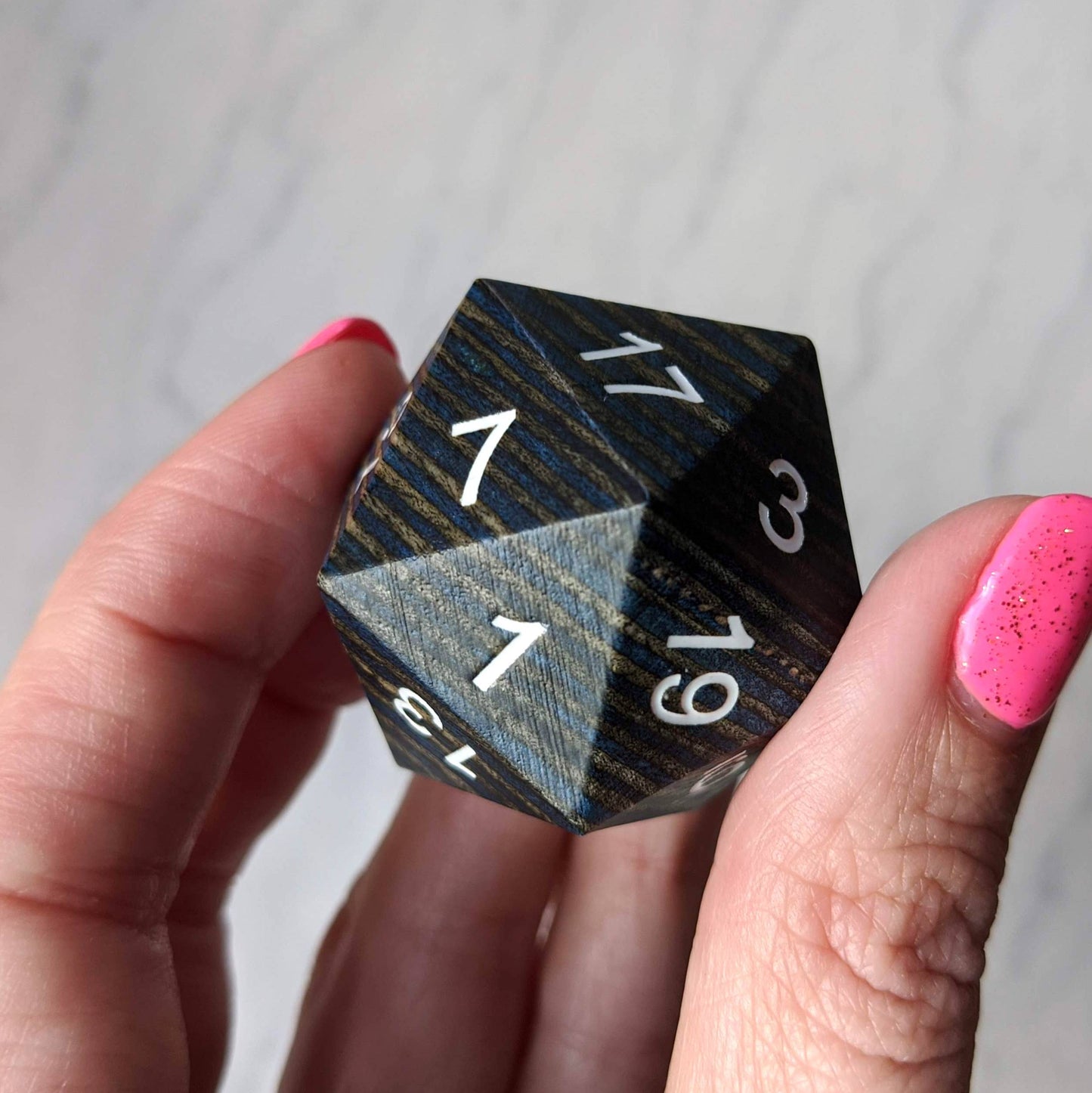 Hand holding a large dark blue and grey striped wooden D20 dice with white numbers, perfect for collectors and gaming enthusiasts.