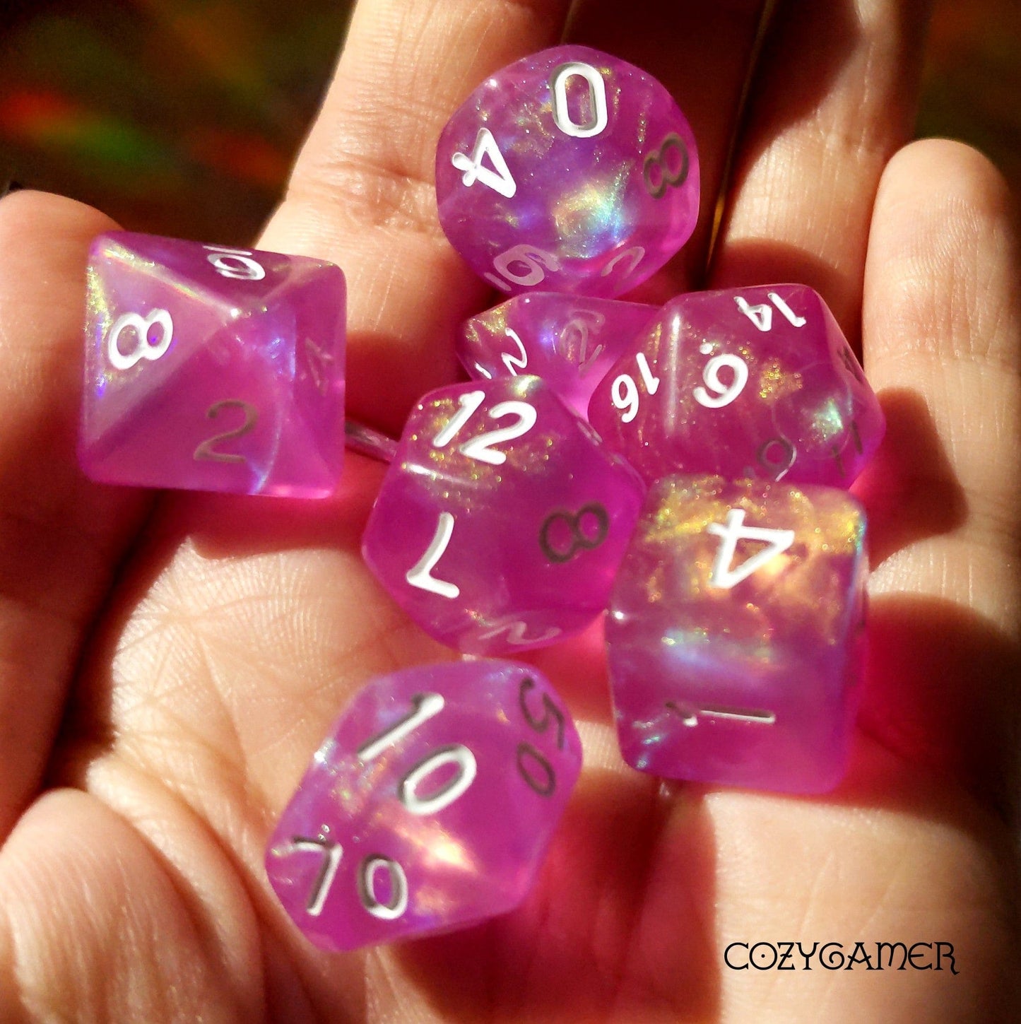 Bright pink shimmering Dream in Bloom dice set for TTRPG, including D20, D12, D10, D%, D8, D6, D4 on hand.