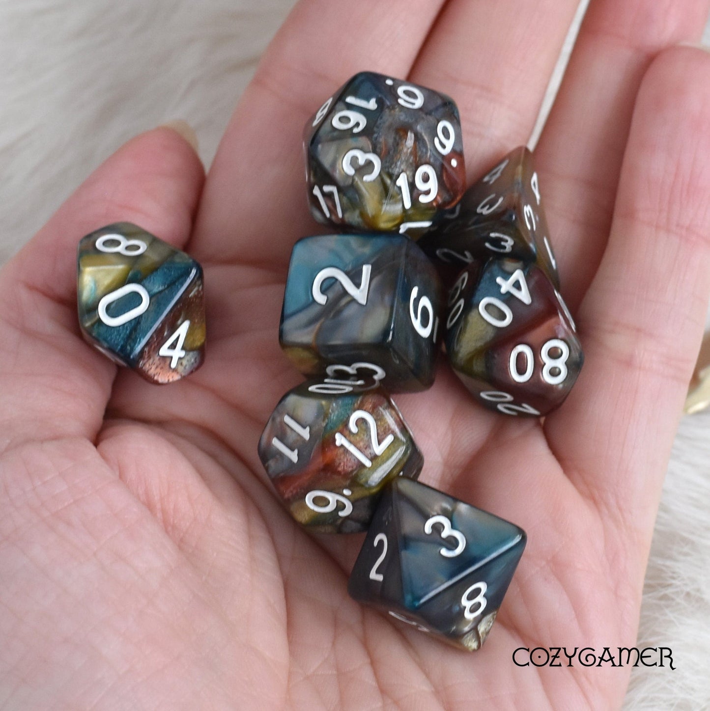 Person holding Earthen Ring Marble Dice Set in pearly blue, burgundy, green, and grey for tabletop RPGs like Dungeons and Dragons.