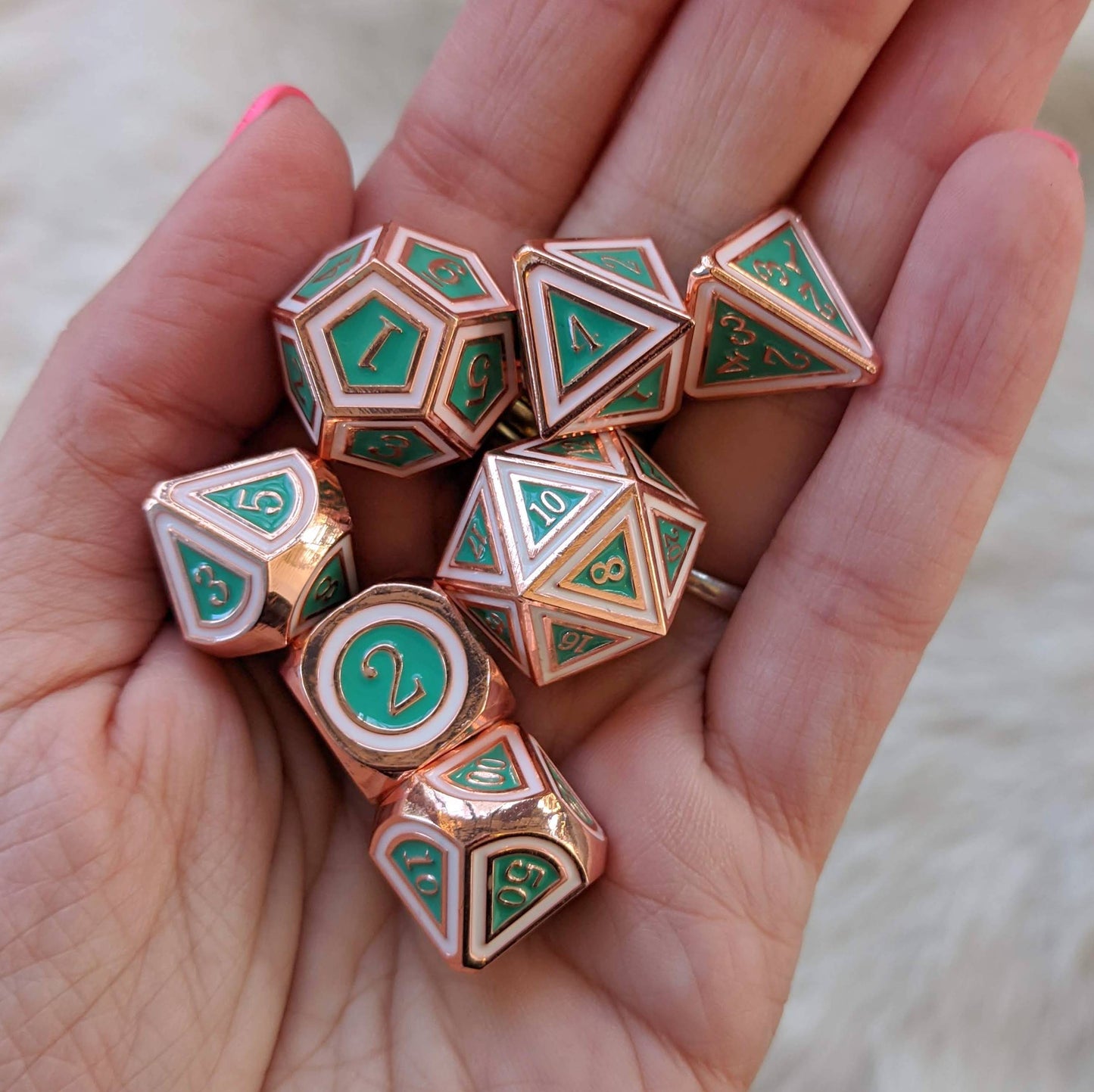 Hand holding Eternal Metal Dice Set, copper plated with turquoise green and white enamel, 7-piece set for tabletop RPGs.