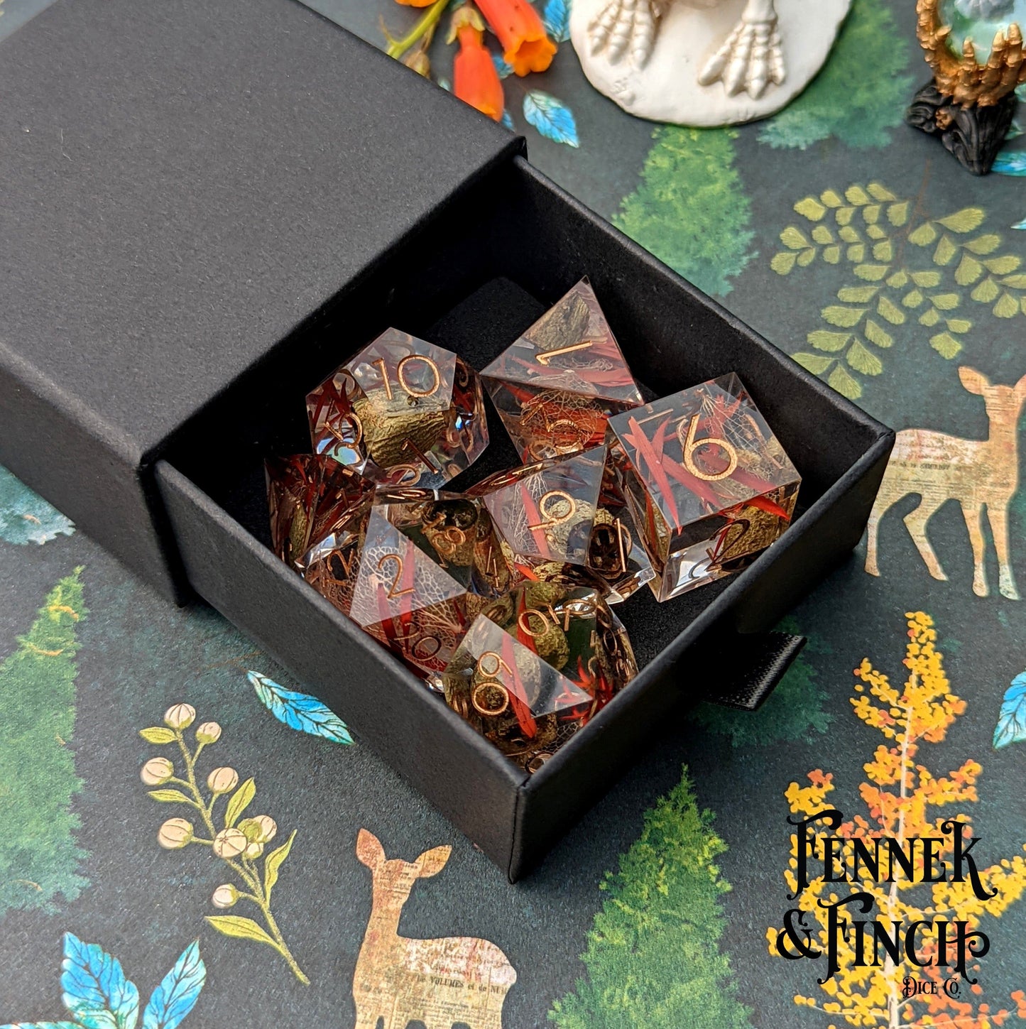 Eucalyptus Sharp Edge Resin Dice Set with Dried Botanicals in Black Box on Colorful Forest-themed Background.