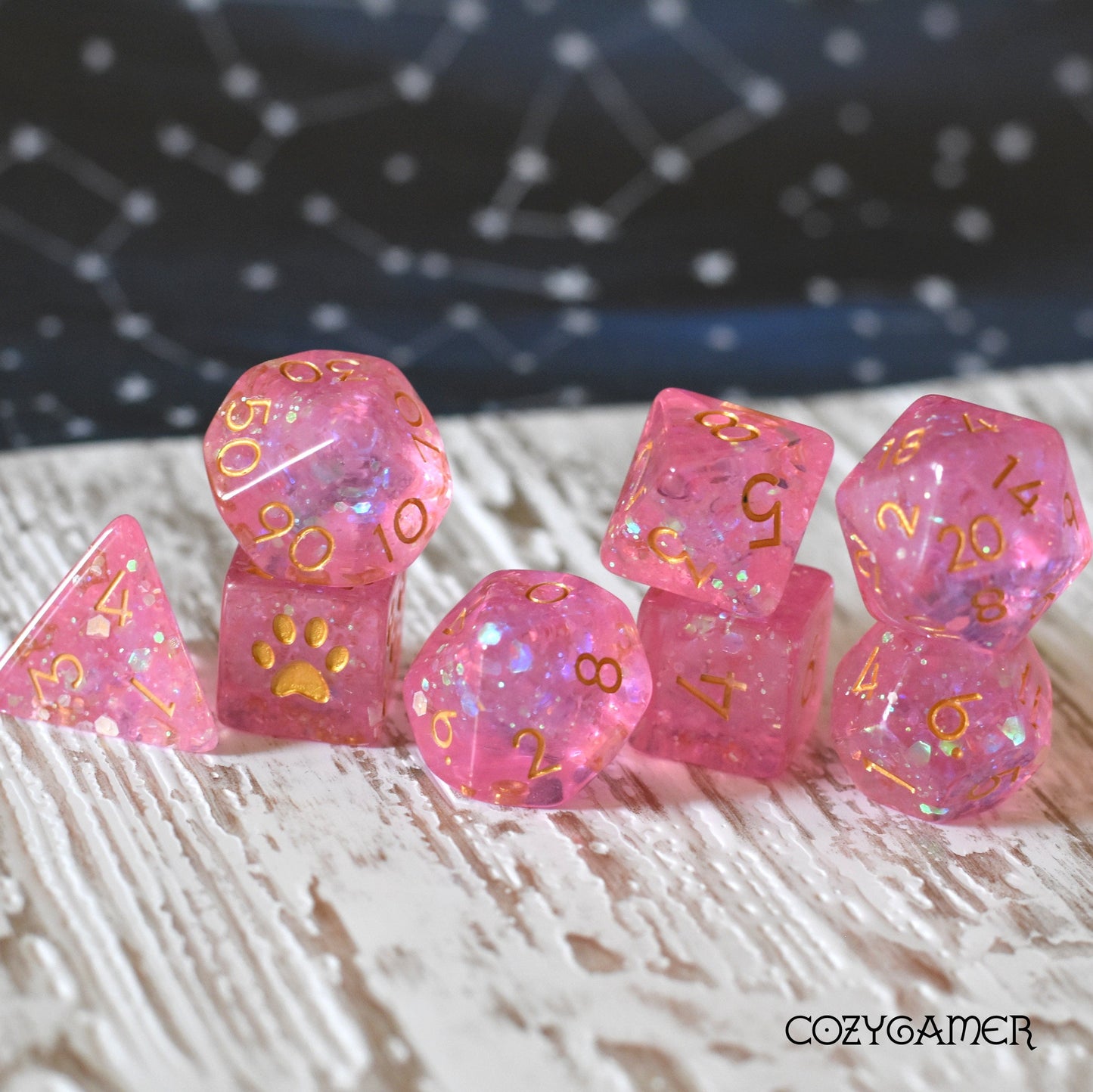 Pink iridescent DnD dice set with custom cat paw D6, featuring numbered polyhedral dice, displayed on a wooden surface.