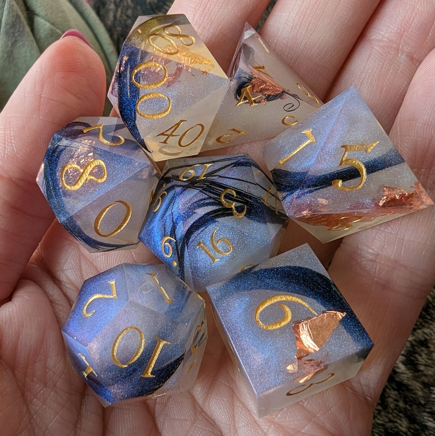 Hand holding Feather Fall 7-piece DnD dice set featuring real black feathers, copper foil, and misty blue effect for tabletop games.