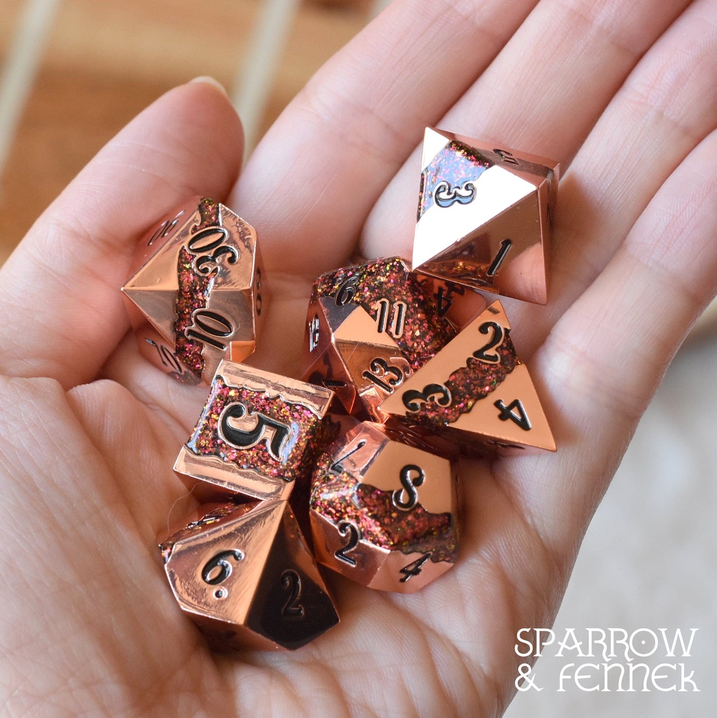 Hand holding Fissure Metal Dice Set in copper with red glitter stripe, 7-piece polyhedral dice for tabletop games like Dungeons and Dragons