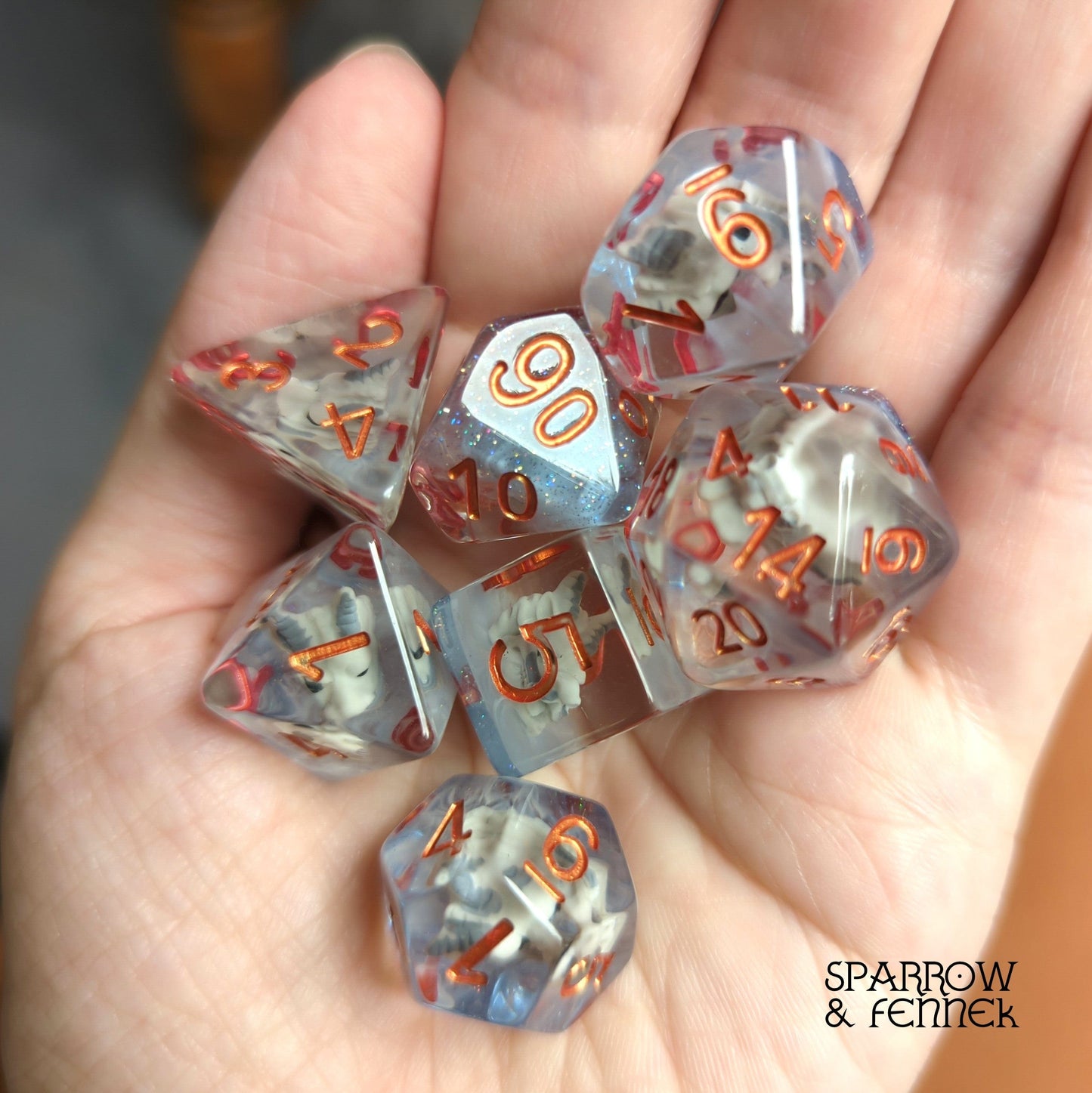Translucent Frost Dragon Dice Set with dragon skulls, held in hand, perfect for Dungeons and Dragons tabletop games.