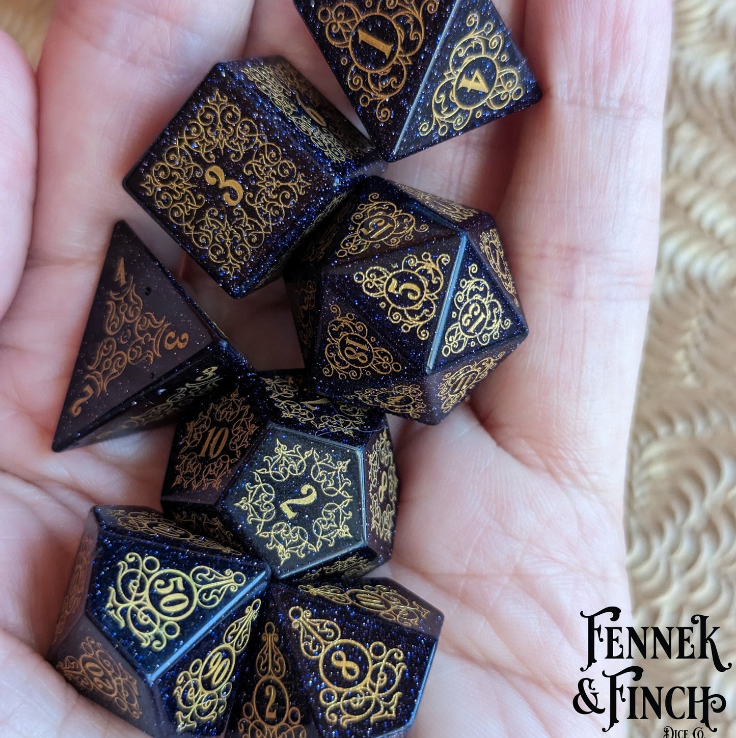 Hand holding Garden Gate Blue Sandstone Gemstone Dice Set with intricate golden designs and shimmering blue stones.