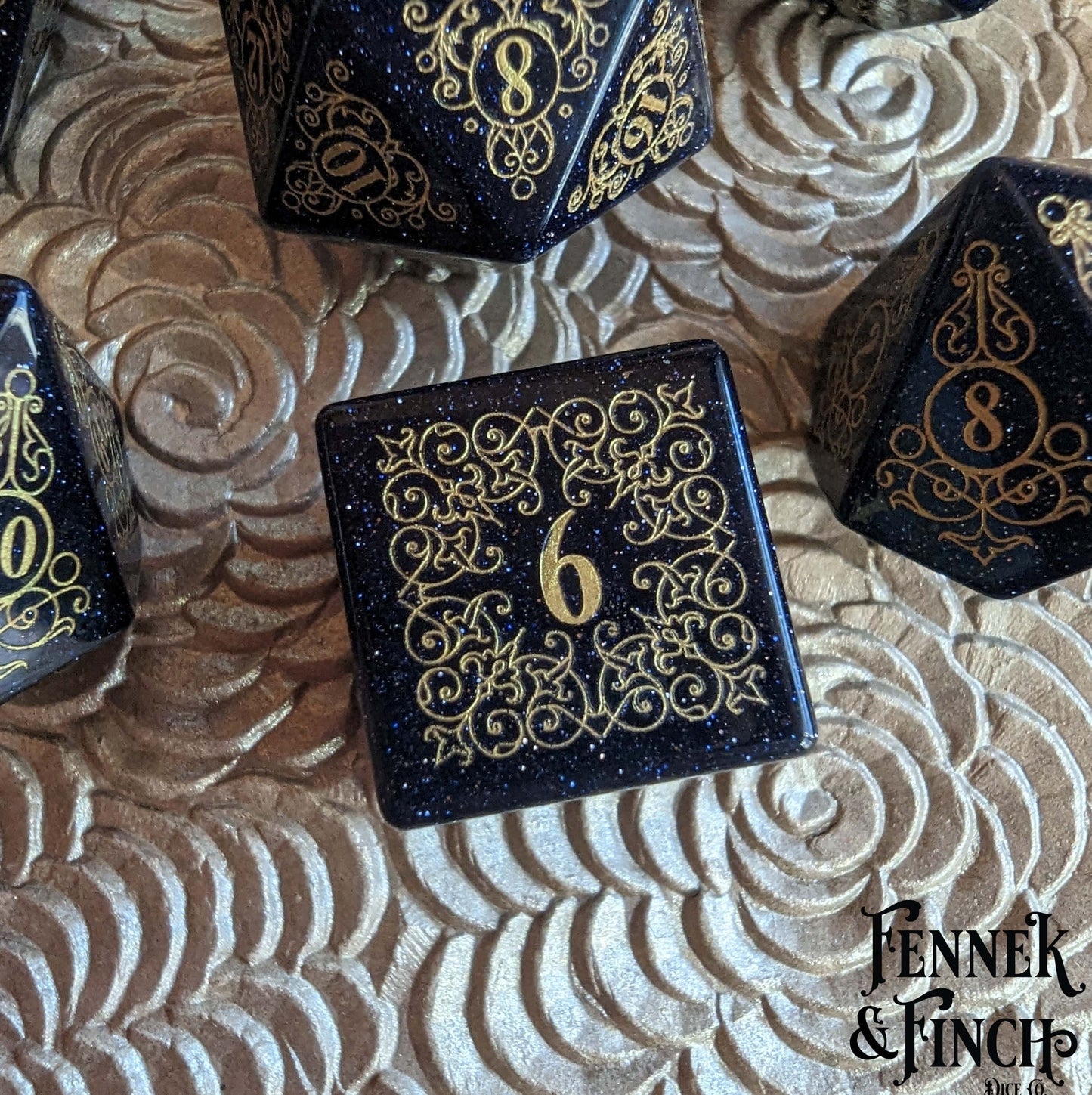 Garden Gate Blue Sandstone Dice Set with intricate gold designs and shimmering dark blue hue on a textured surface.