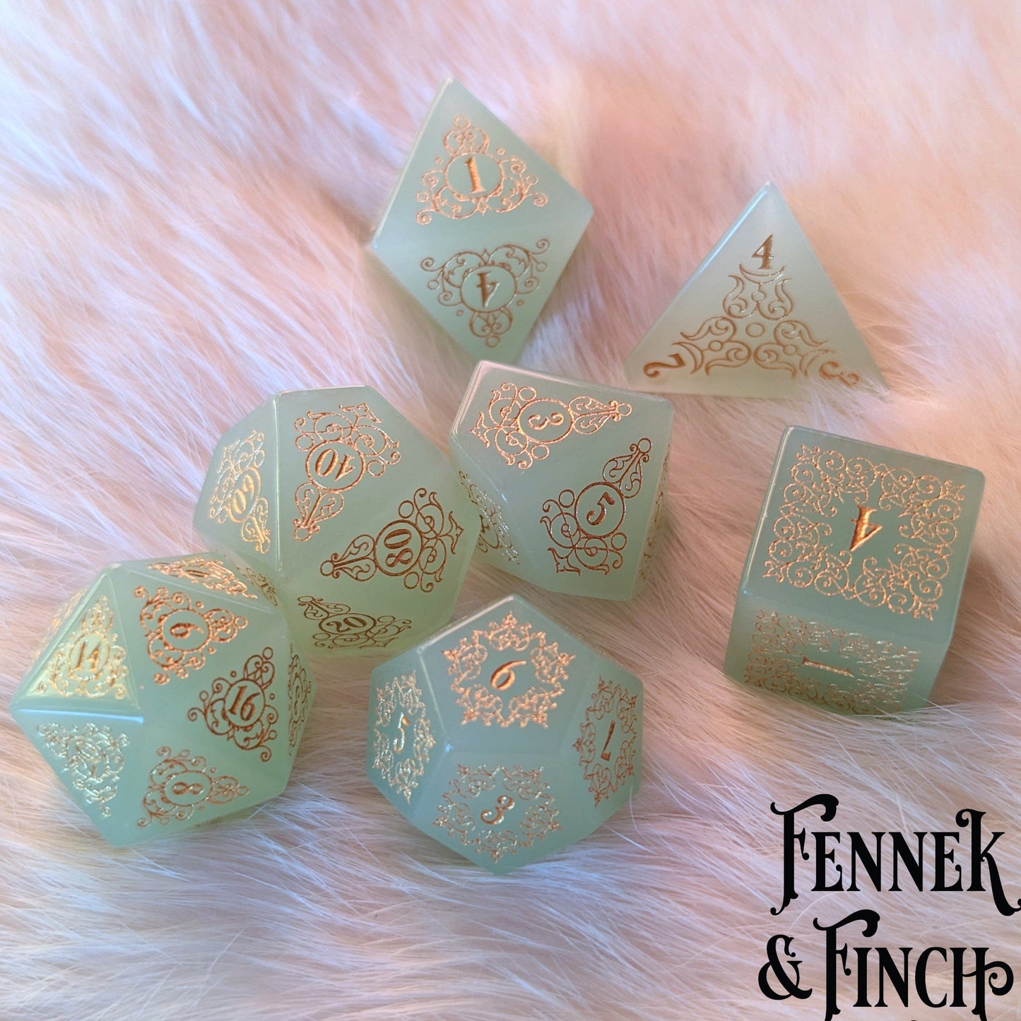 Milky green glass gemstone dice set with intricate floral designs on white fur background.