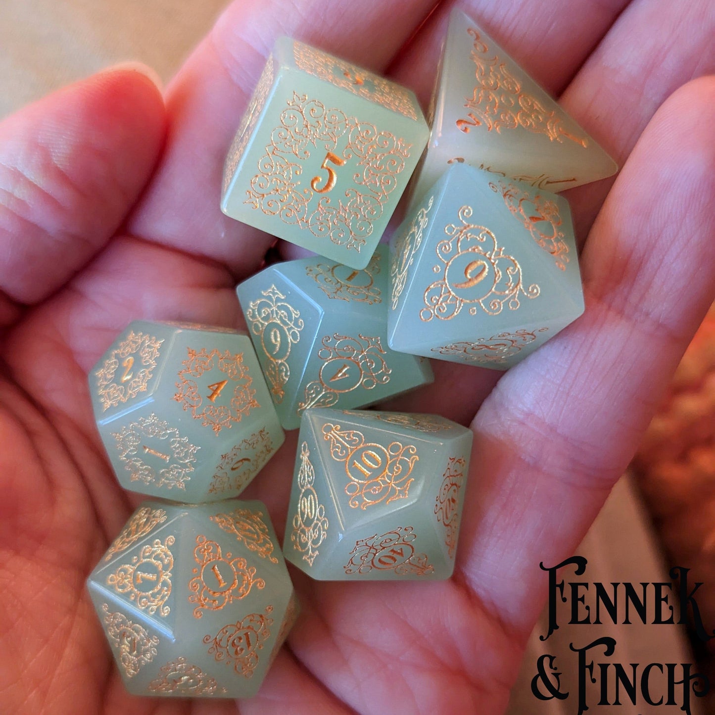 Milky green glass gemstone dice set with intricate floral designs, held in hand, by Fennek & Finch.