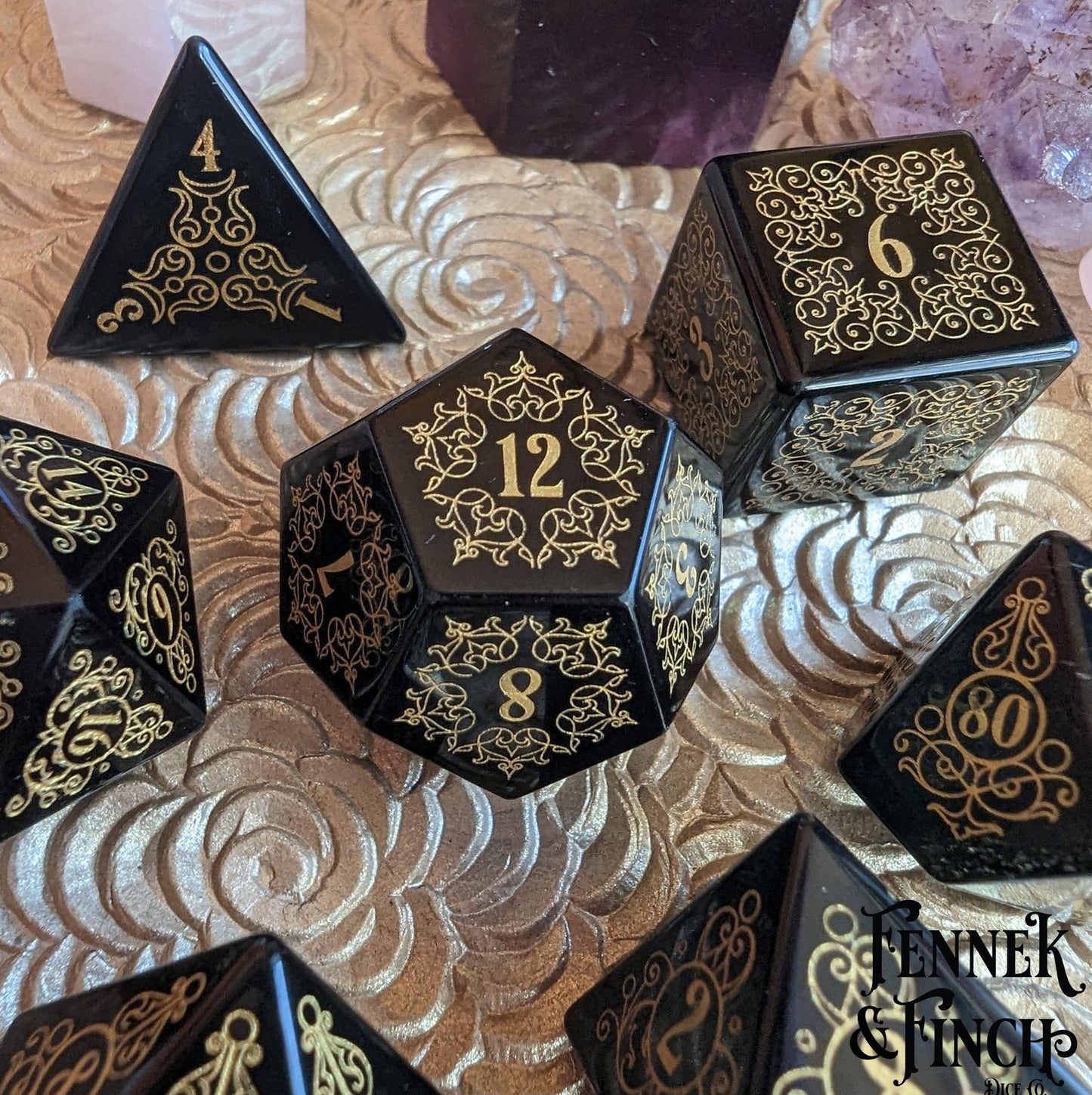 Obsidian gemstone dice set with intricate floral designs and gold numbers on a decorative surface.
