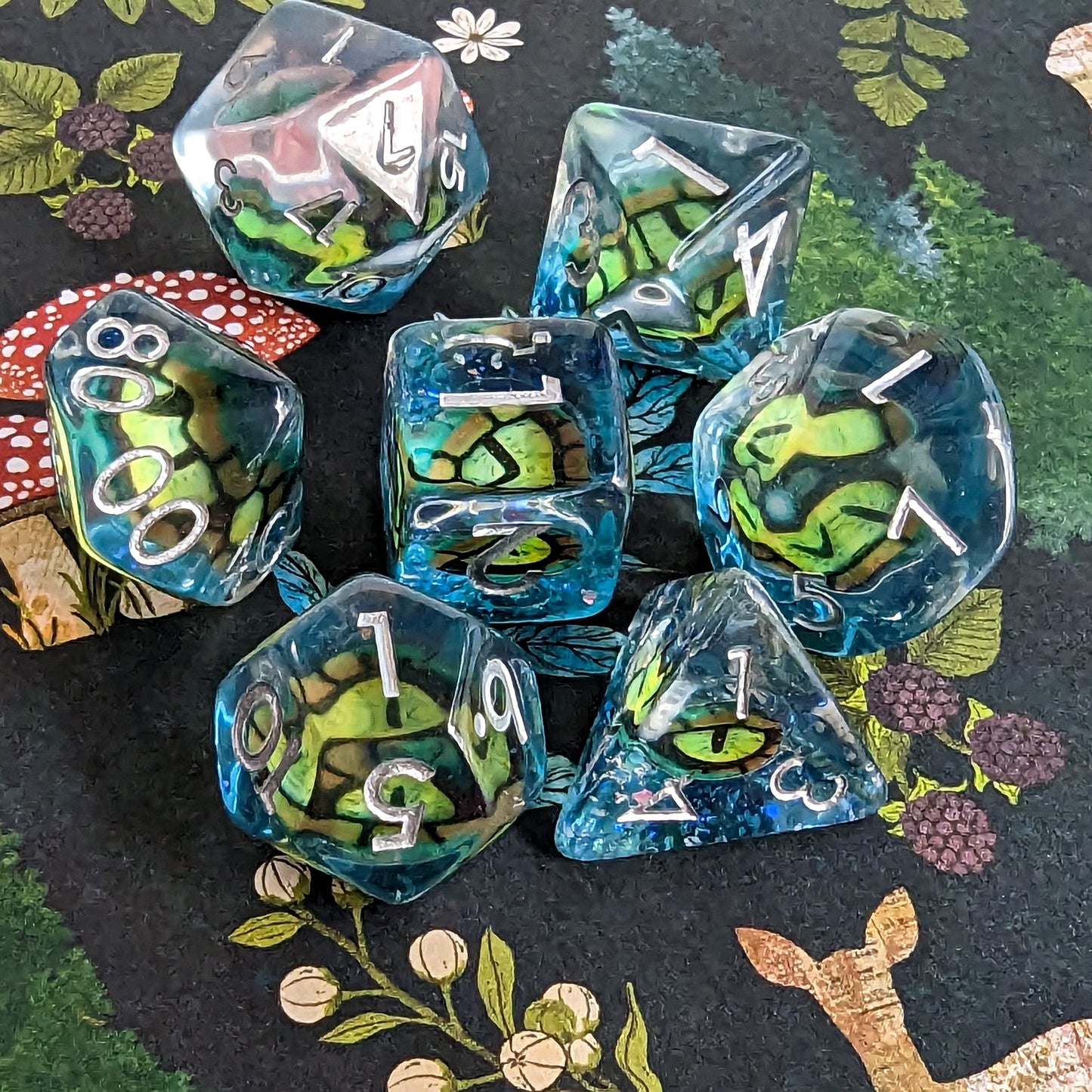 Green Eye DnD Dice Set with detailed eye designs on blue polyhedral dice for tabletop role-playing games, surrounded by nature-themed background.