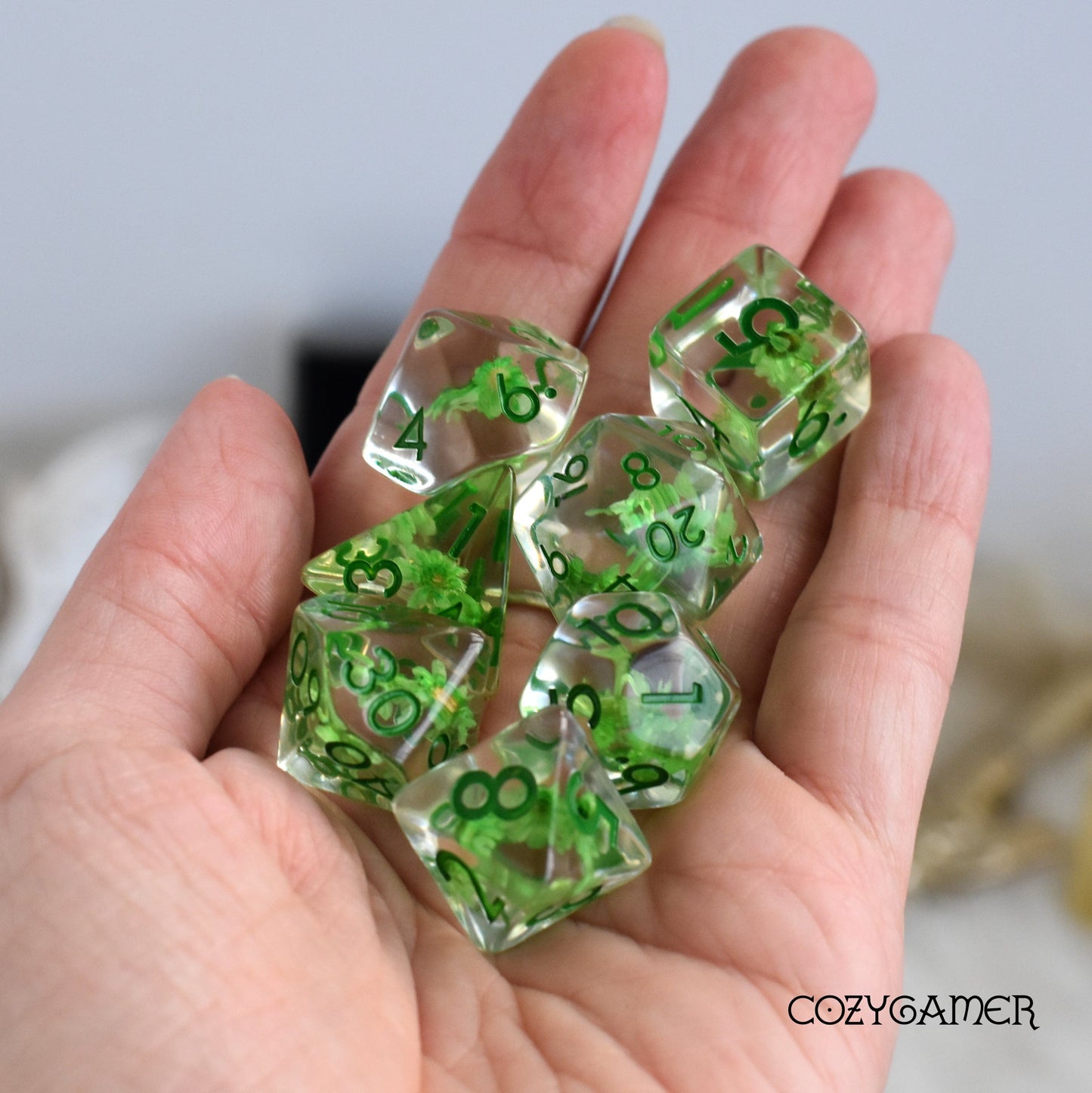 Hand holding green mini flower dice set for tabletop games, featuring resin dice with dried flowers and green numbers.