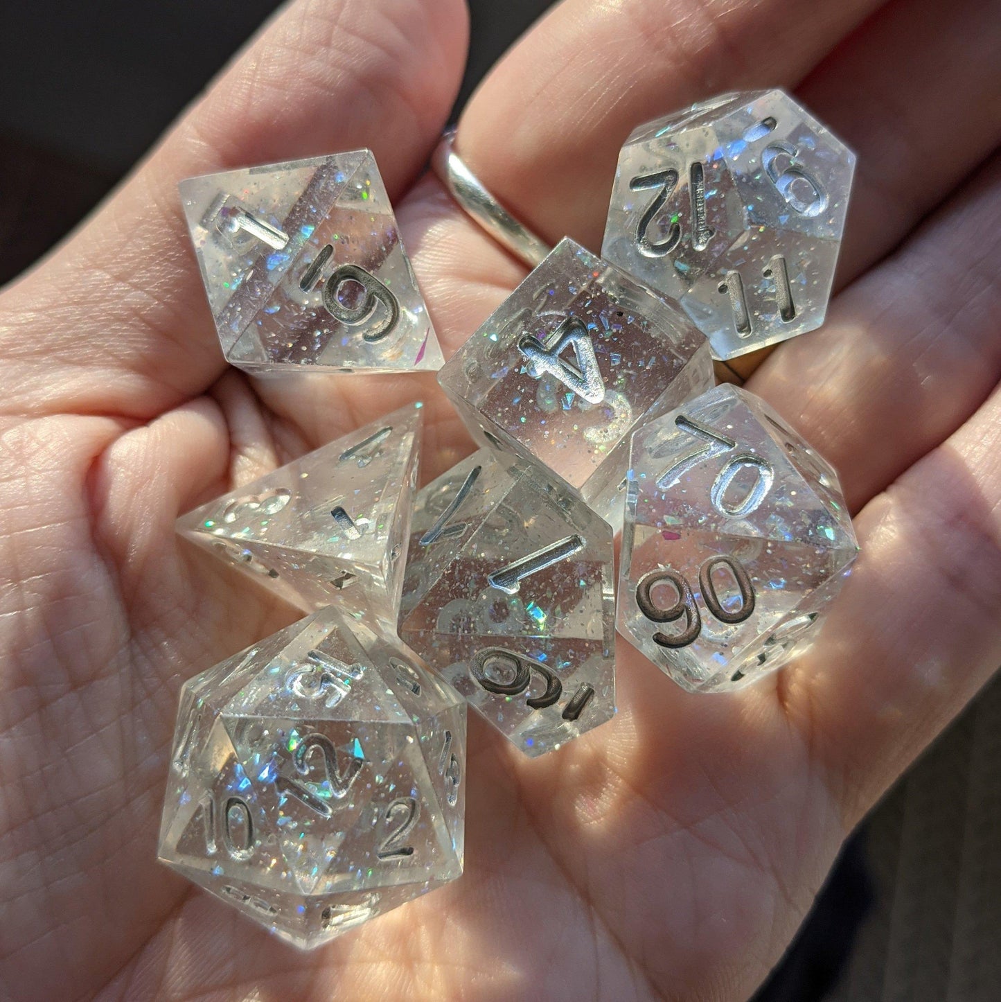 Hand holding Ice Palace Sharp Edge Dice Set with opal flakes and silver numbers, perfect for Dungeons and Dragons and TTRPGs.