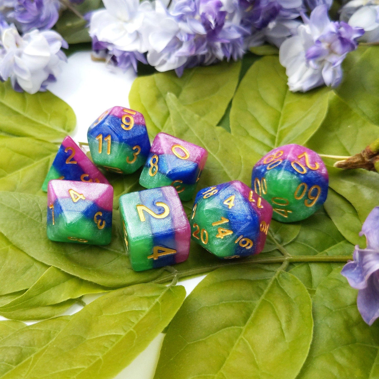 Jester's Gambit Dice Set, layered in pearly pink, blue, and green with gold numbers, perfect for tabletop RPGs like Dungeons and Dragons.