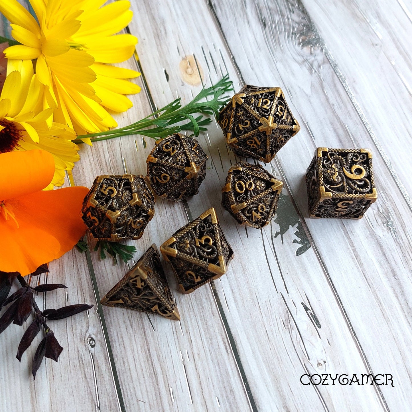Kraken Hollow Metal Dice Set on wooden surface with yellow and orange flowers in the background, perfect for tabletop RPGs.