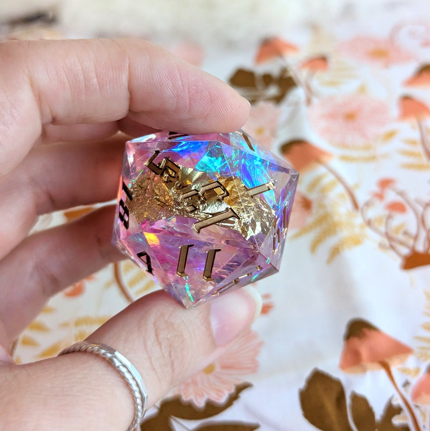 Hand holding a large sharp edge D20 resin die with iridescent colors for Dungeons and Dragons tabletop games.