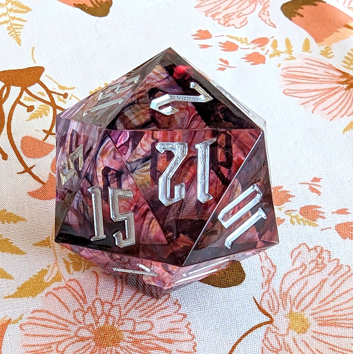 Large 33mm purple sharp edge resin D20 die for Dungeons and Dragons tabletop games on floral background.
