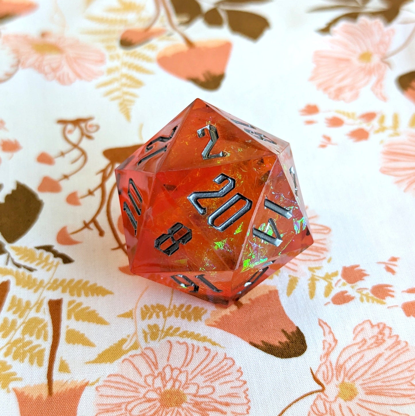 Large orange sharp-edge resin D20 die for Dungeons and Dragons on a floral background, perfect for tabletop RPG games.