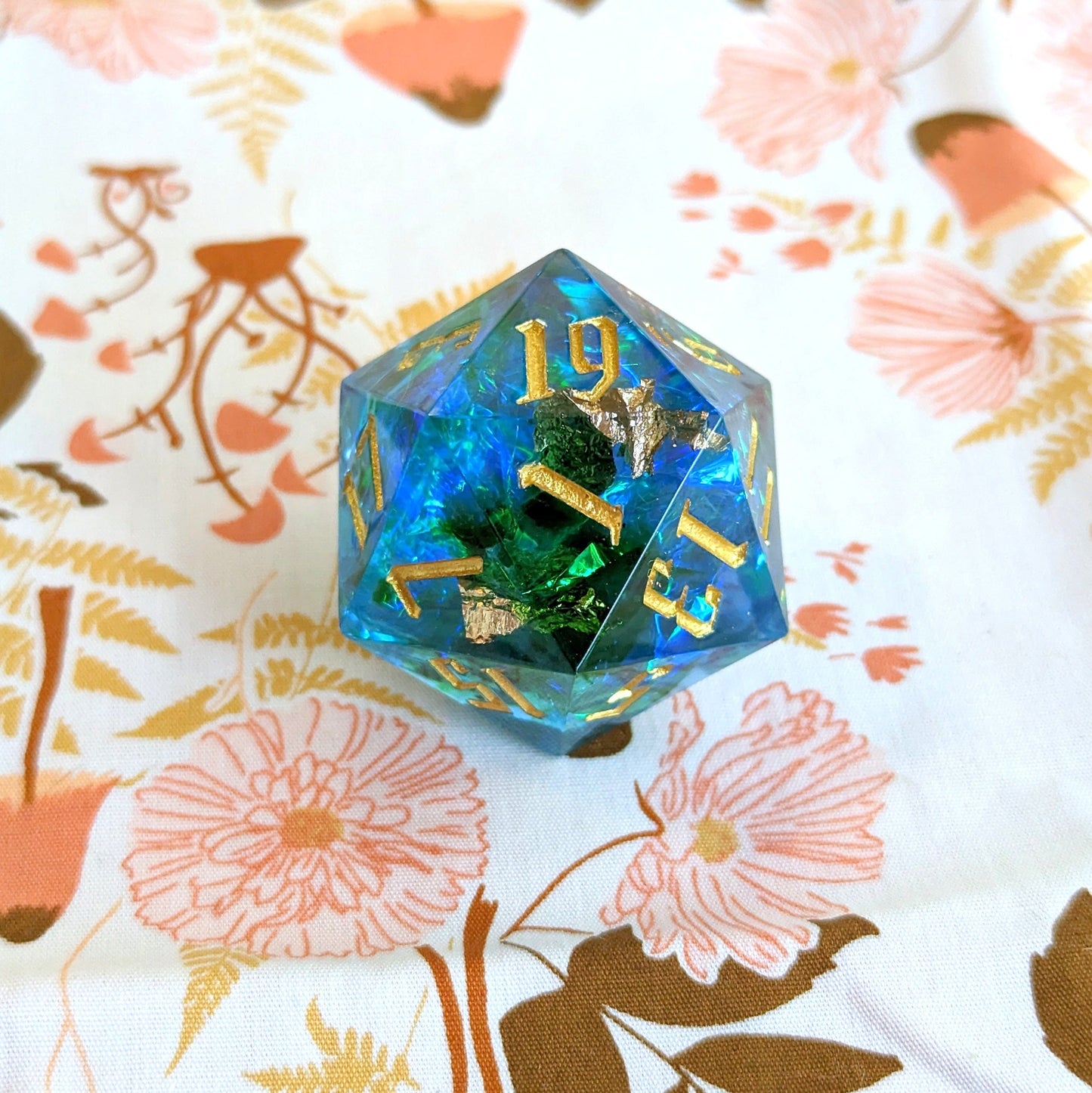 Large blue resin D20 die with gold numbers for DnD and tabletop RPGs on floral background.